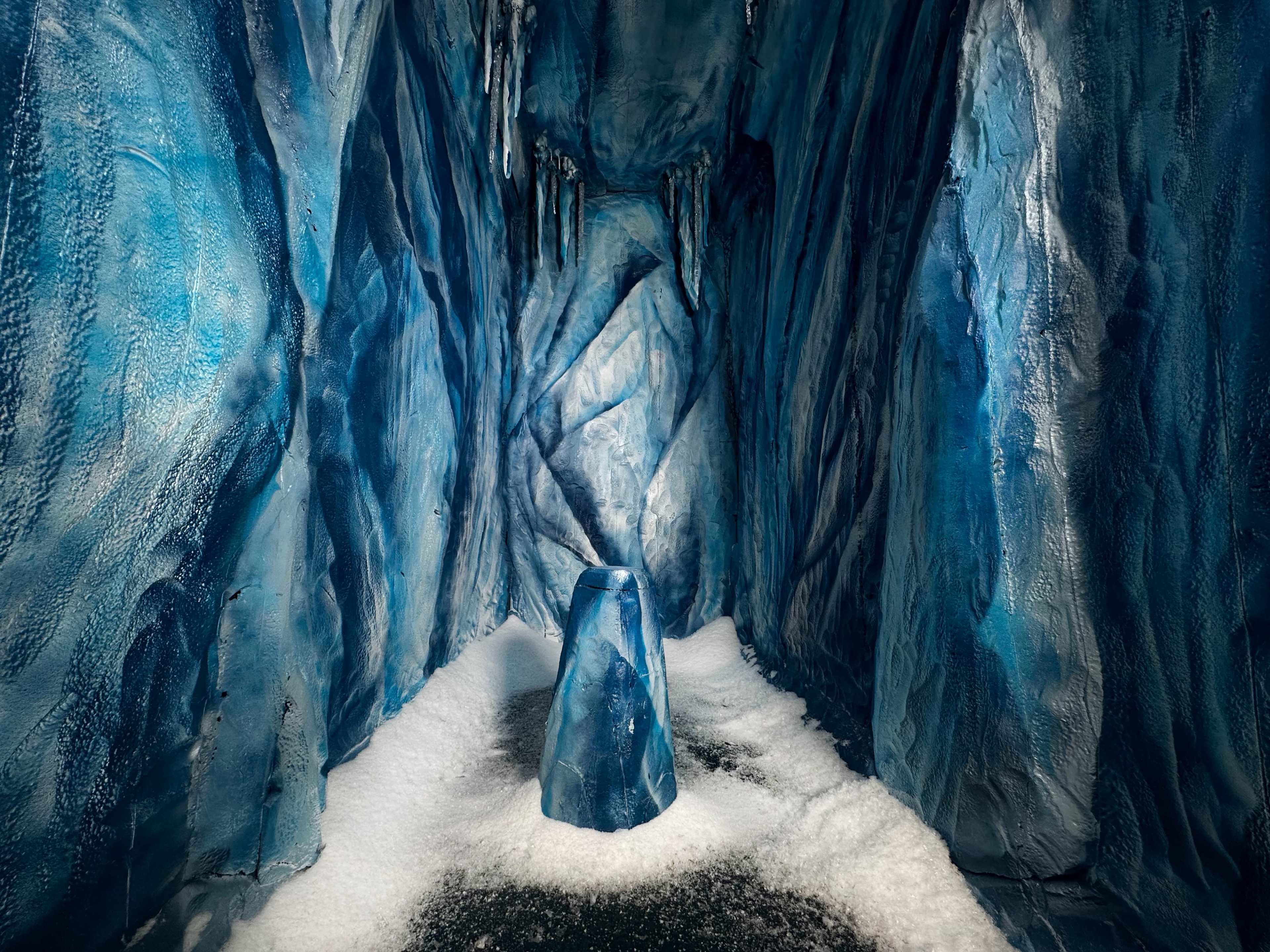A cave-like space with blue and white textured walls resembling ice, and a central ice-shaped sculpture surrounded by a layer of white material.