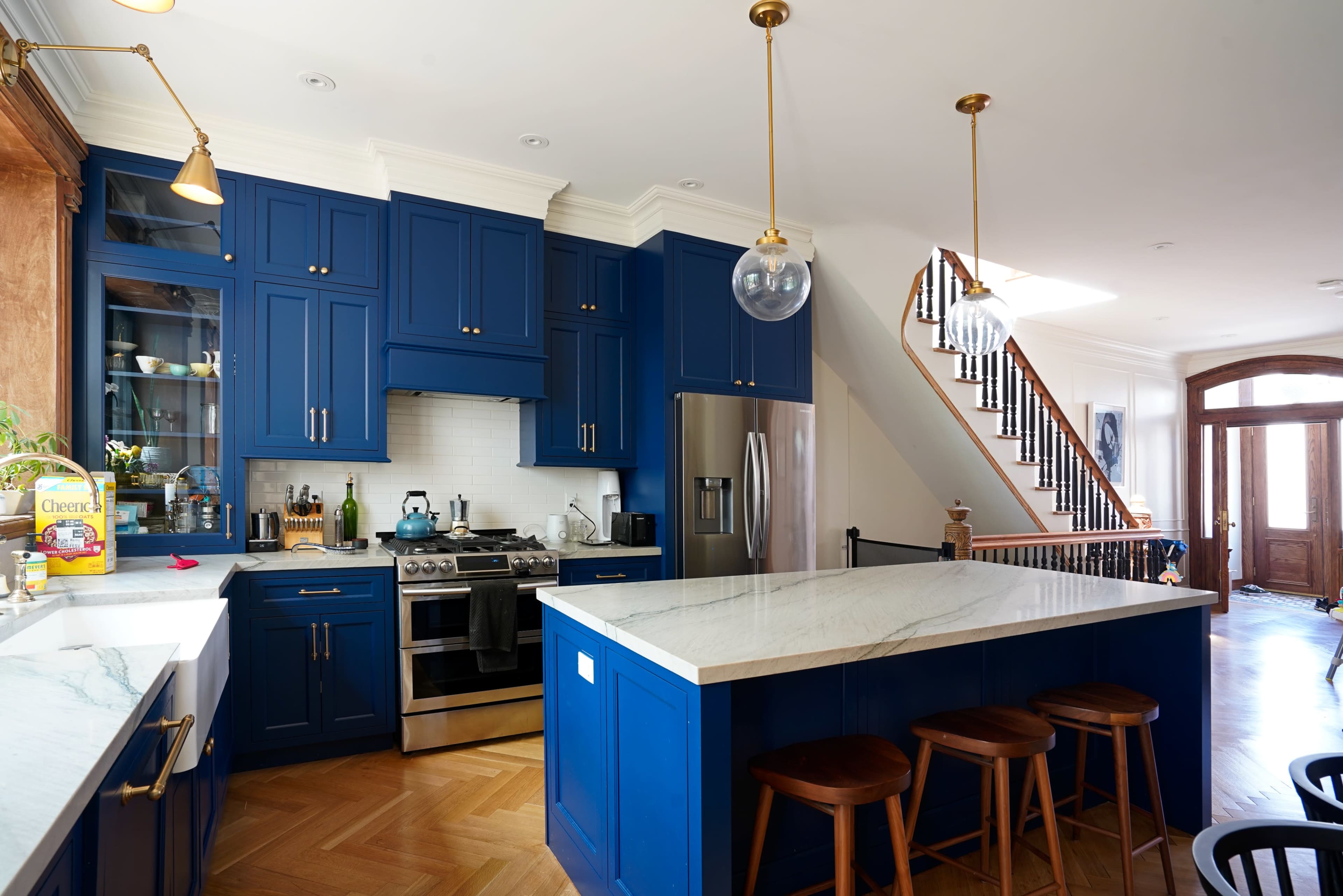 The kitchen features blue cabinetry, stainless steel appliances, and a large marble countertop island, with an adjacent staircase leading to a second floor.