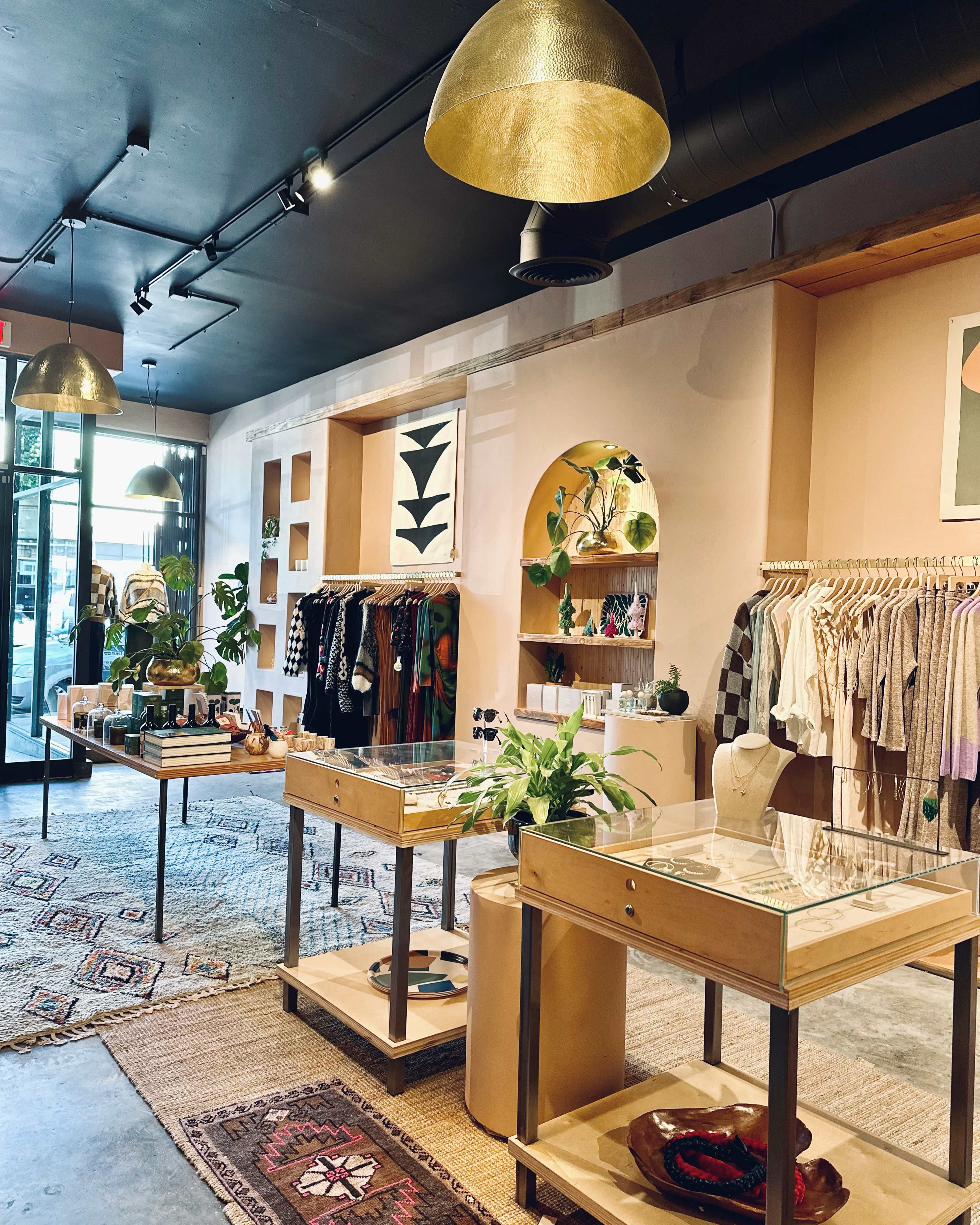 The interior of a boutique features clothing racks, display tables with glass tops, and decorative plants, all set against a chic, colorful backdrop.