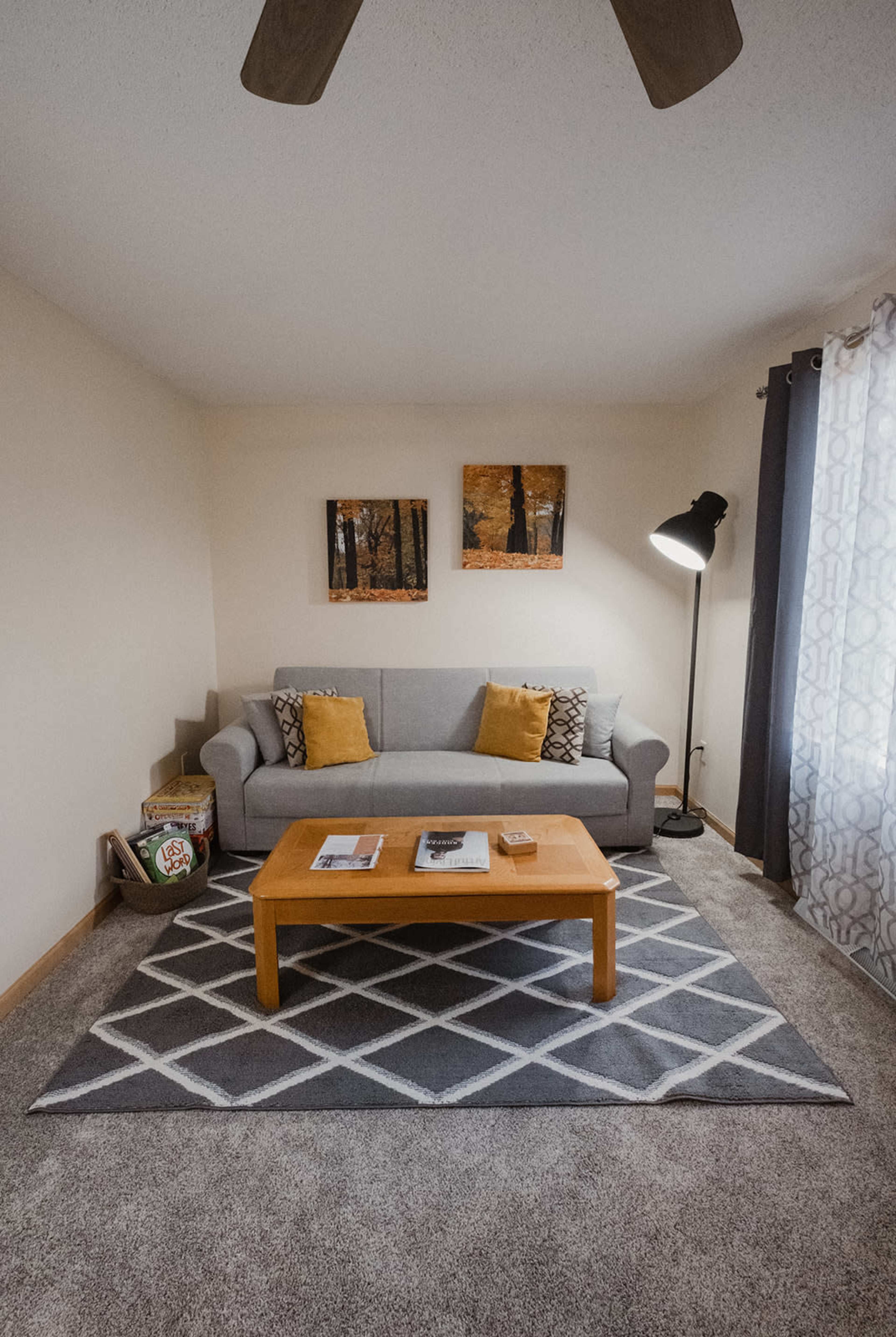 A gray sofa with yellow cushions is positioned next to a wooden coffee table on a patterned rug in a well-lit living room.