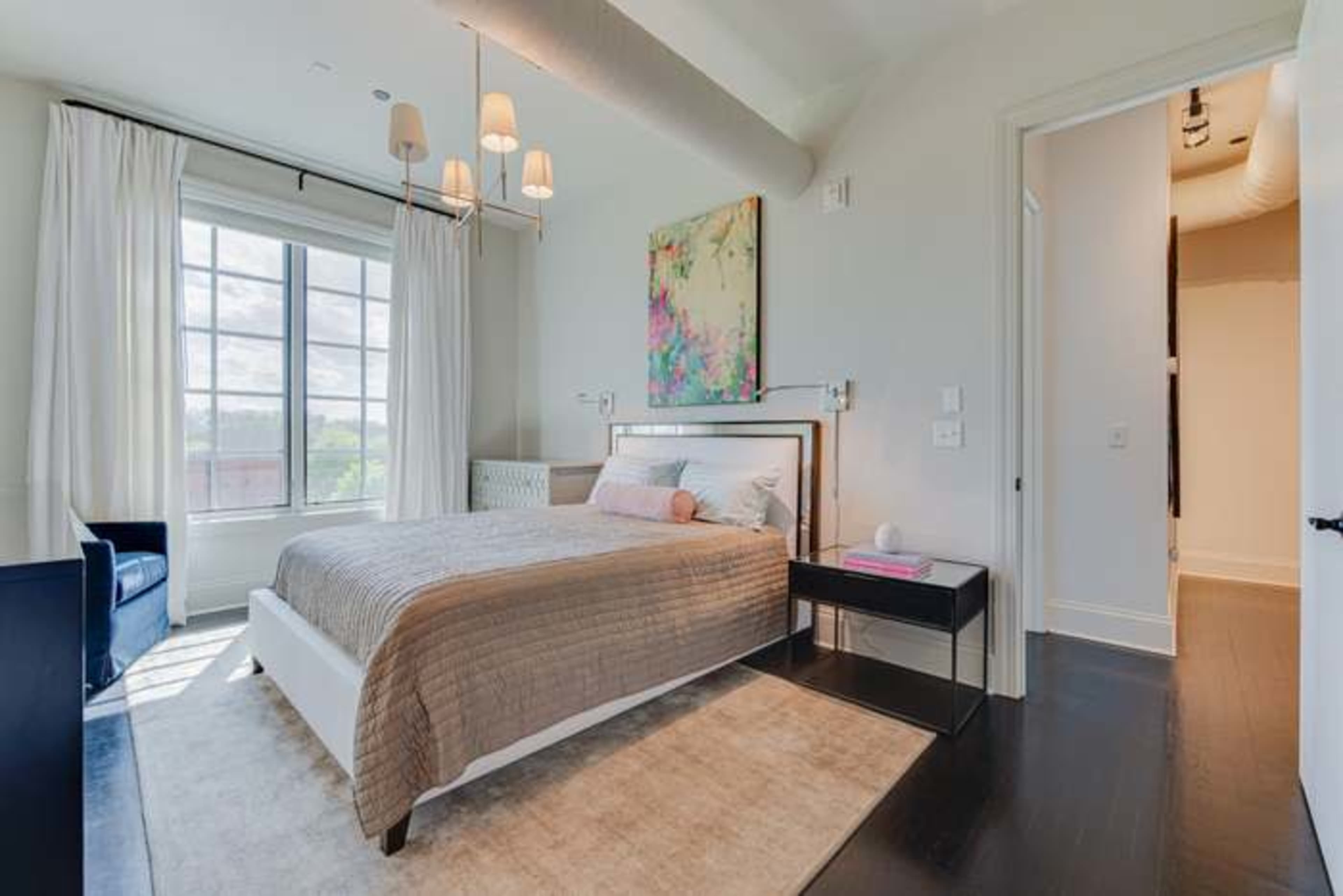The image features a modern bedroom with a bed, nightstand, and large window letting in natural light.