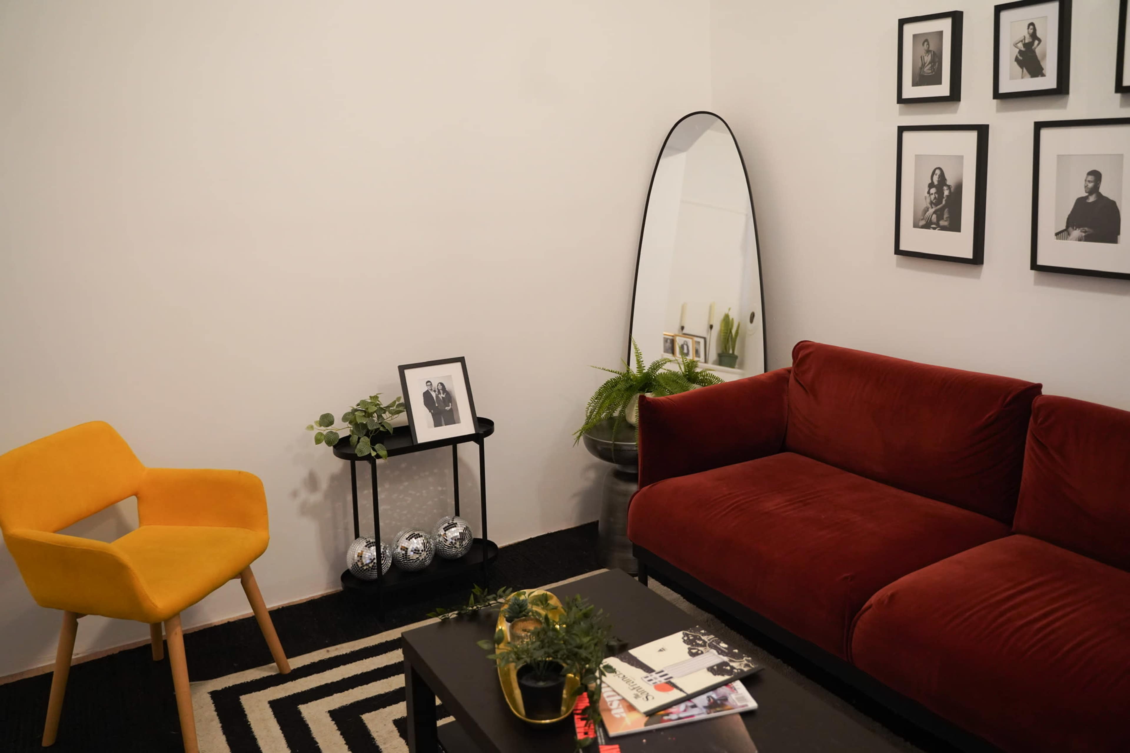 A cozy living room features a red couch, a yellow chair, a black coffee table, and framed black-and-white photographs on the wall.