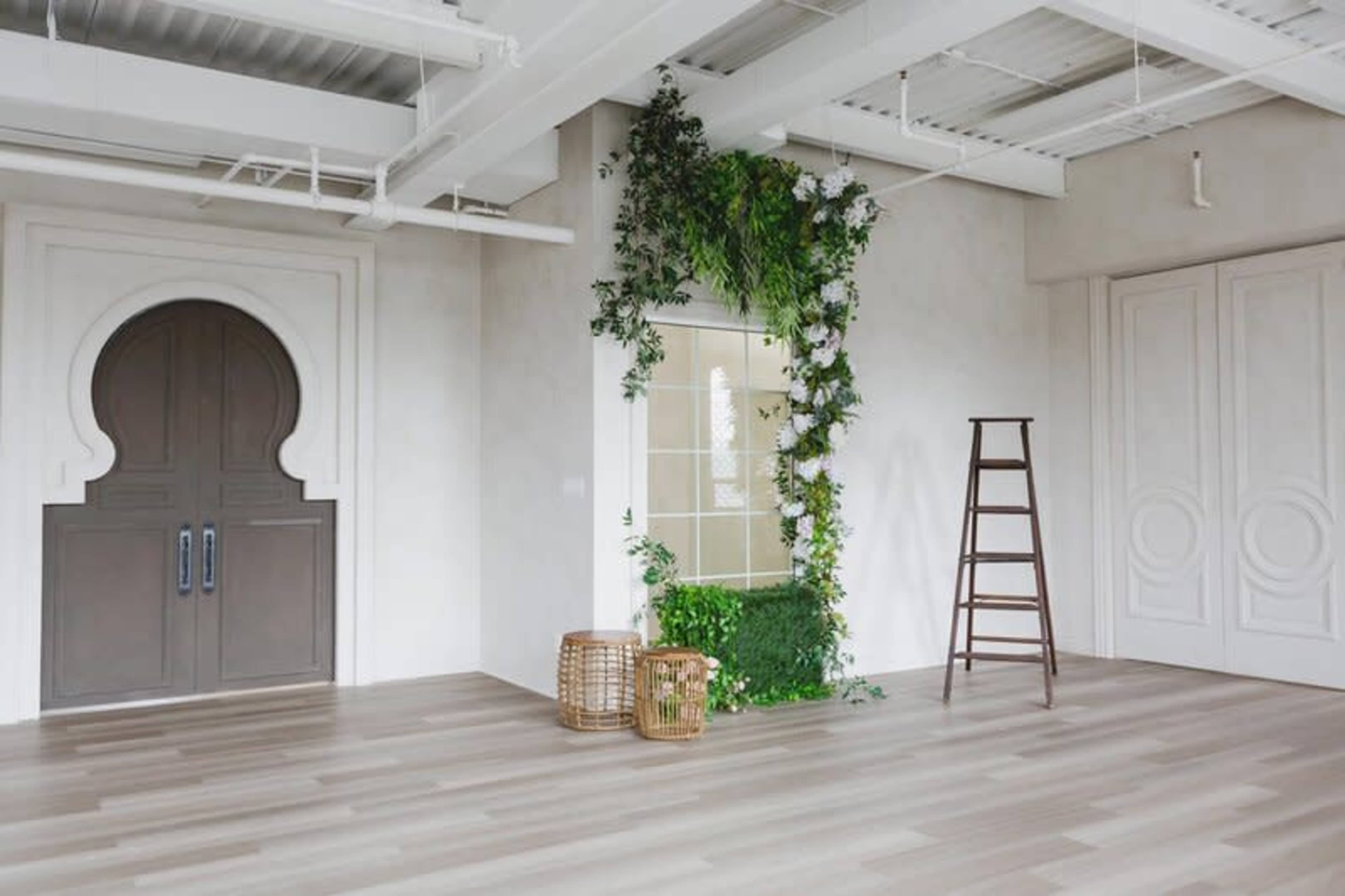 A spacious room featuring a decorative archway, a plant-filled wall, a wooden ladder, and two wicker baskets on the floor.