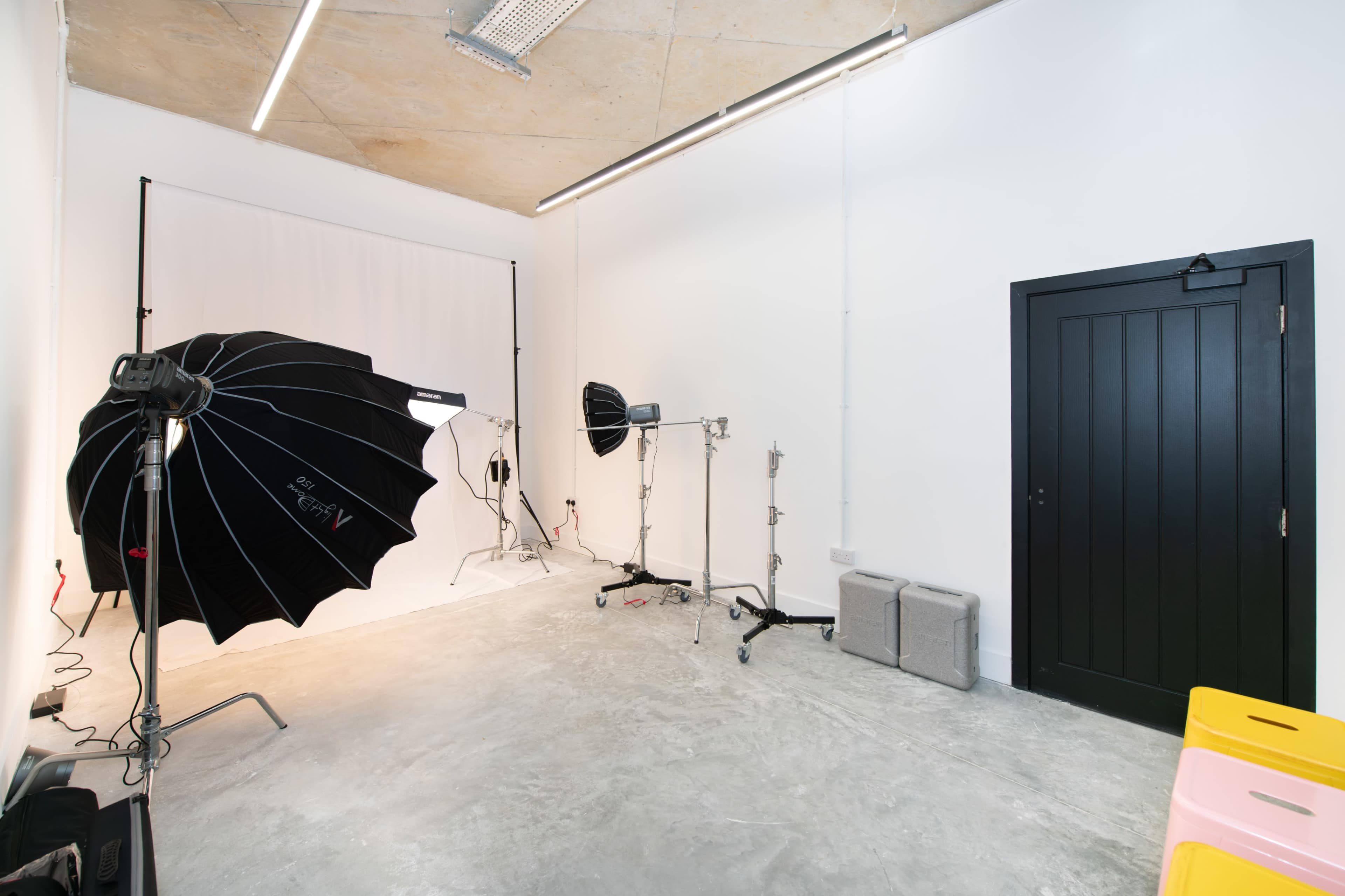 A photography studio with a white backdrop, lighting equipment, and a black door.