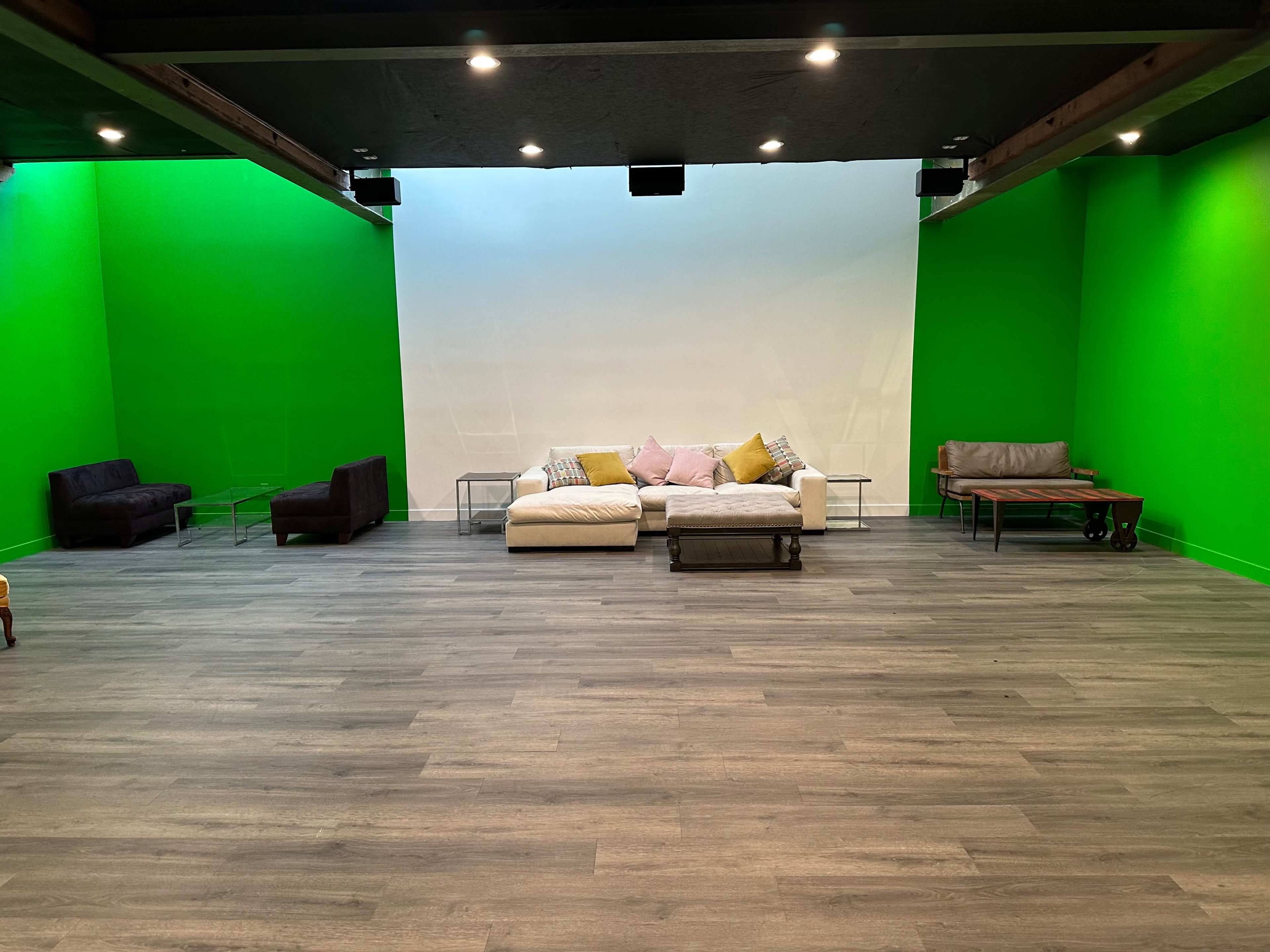 The image shows a room with a bright green wall, featuring various seating arrangements, including a white couch with decorative pillows, two armchairs, and a coffee table on a wooden floor.