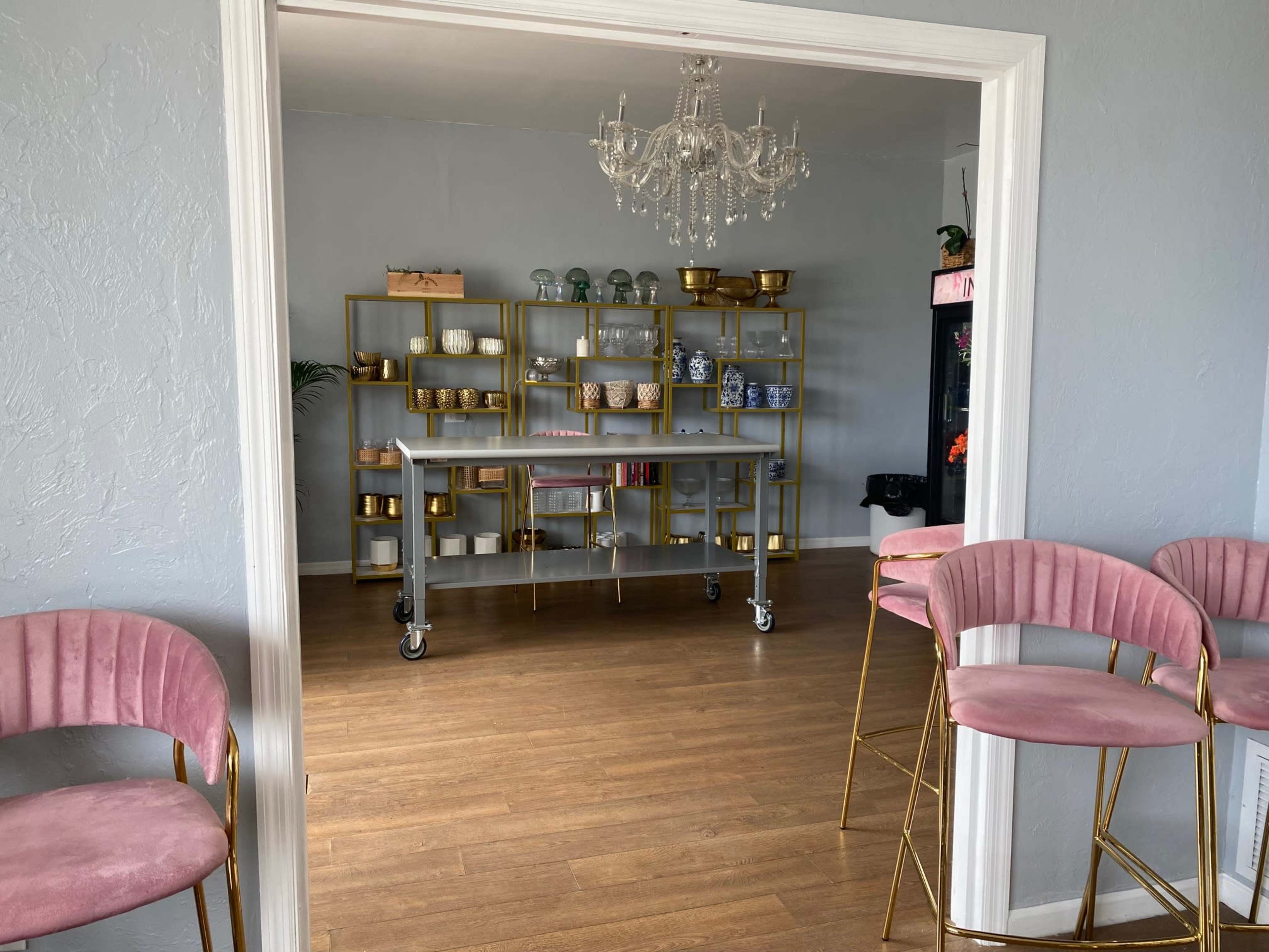 A bright room features a cart with various decorative items and shelves lined with gold and glass bowls, accompanied by pink chairs at the entrance.