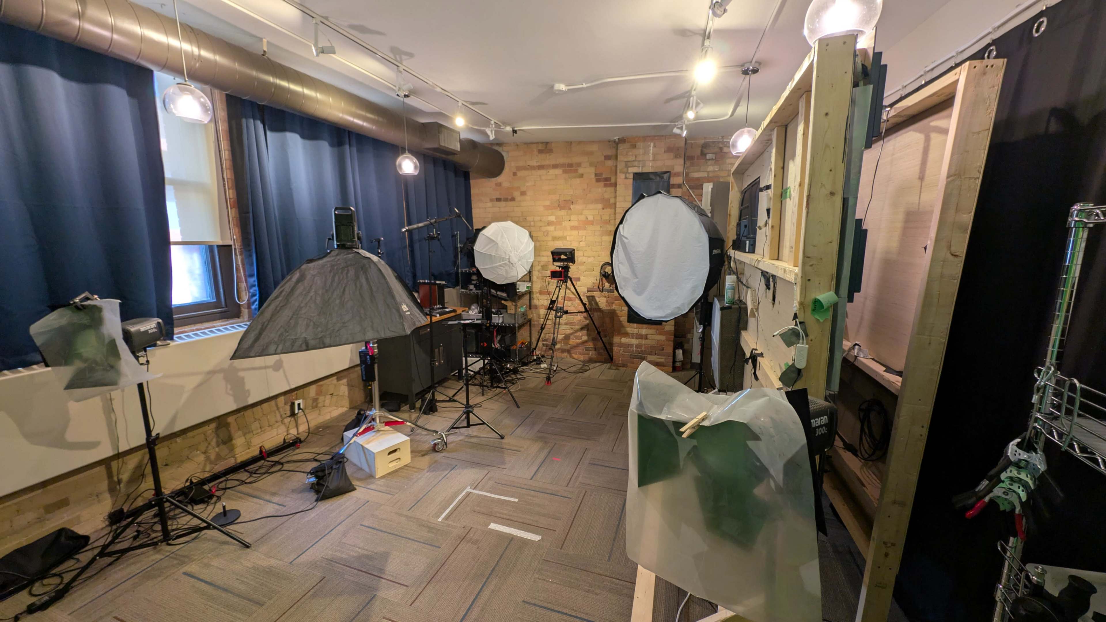 The image shows a photography studio filled with lighting equipment, backdrops, and various setups for shooting.