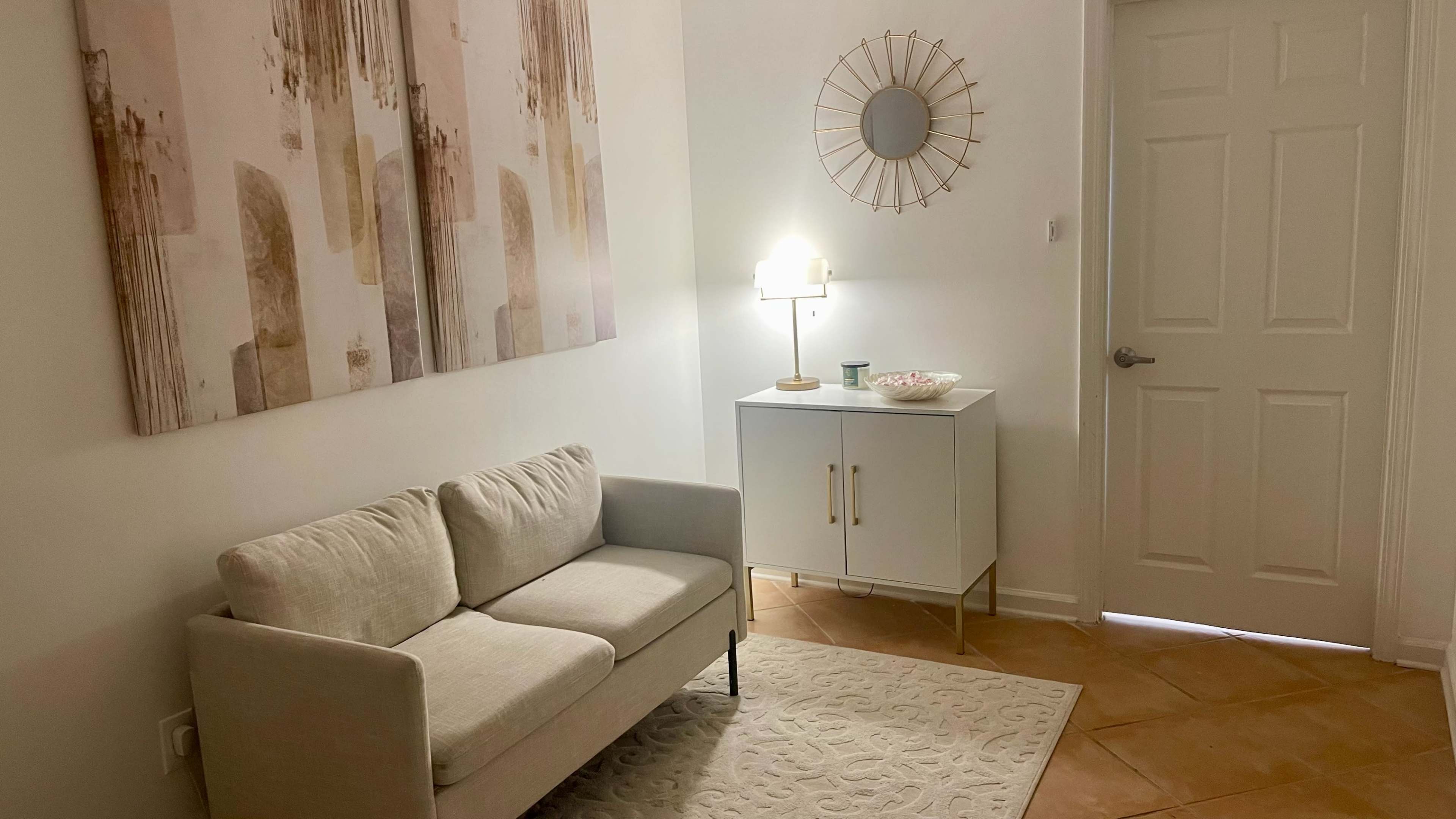 A small, well-lit room featuring a beige couch, a white cabinet, and two large abstract art pieces on the wall.