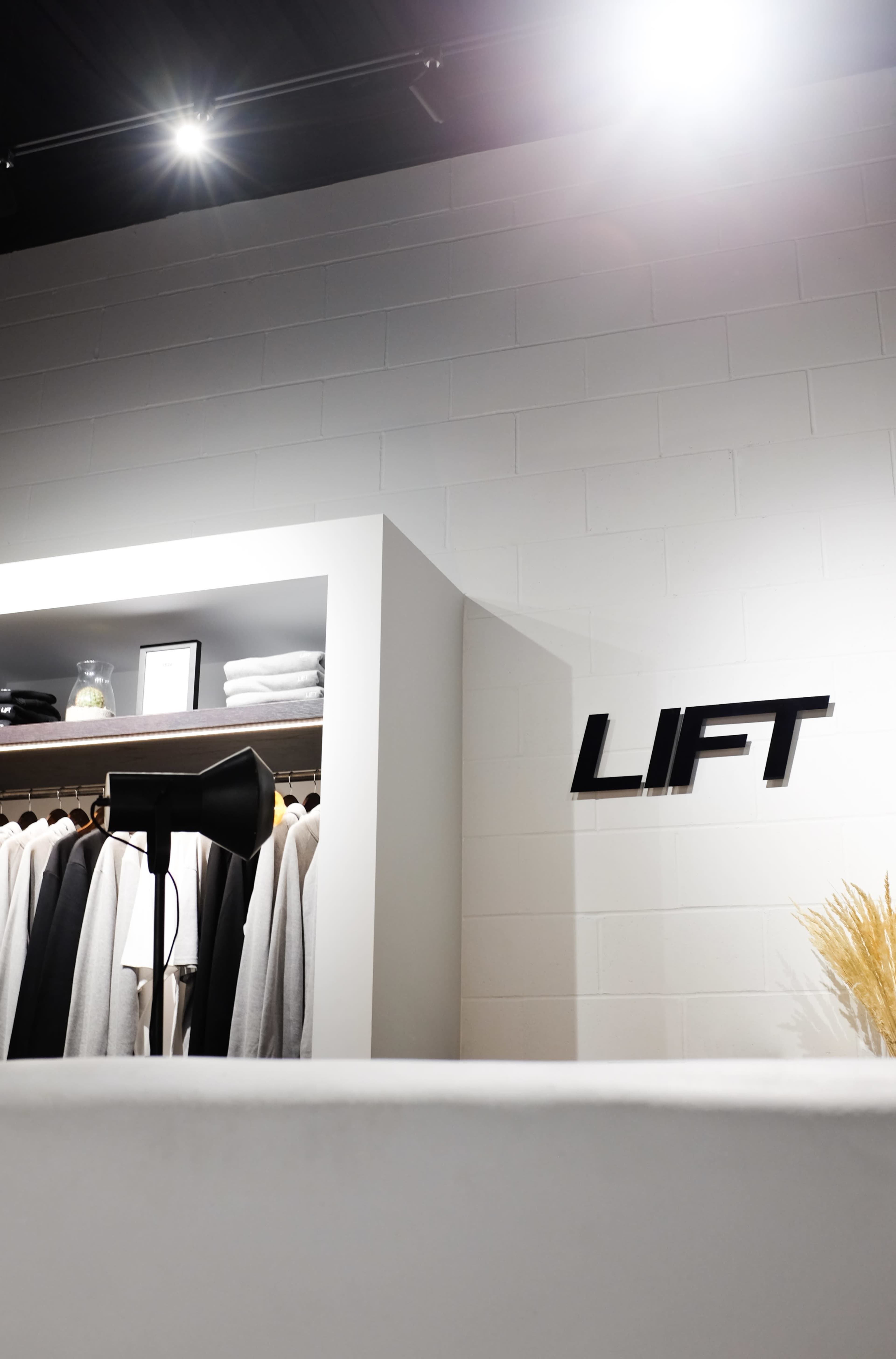 A modern clothing store interior with neatly arranged apparel on hangers and the word "LIFT" displayed on the wall.