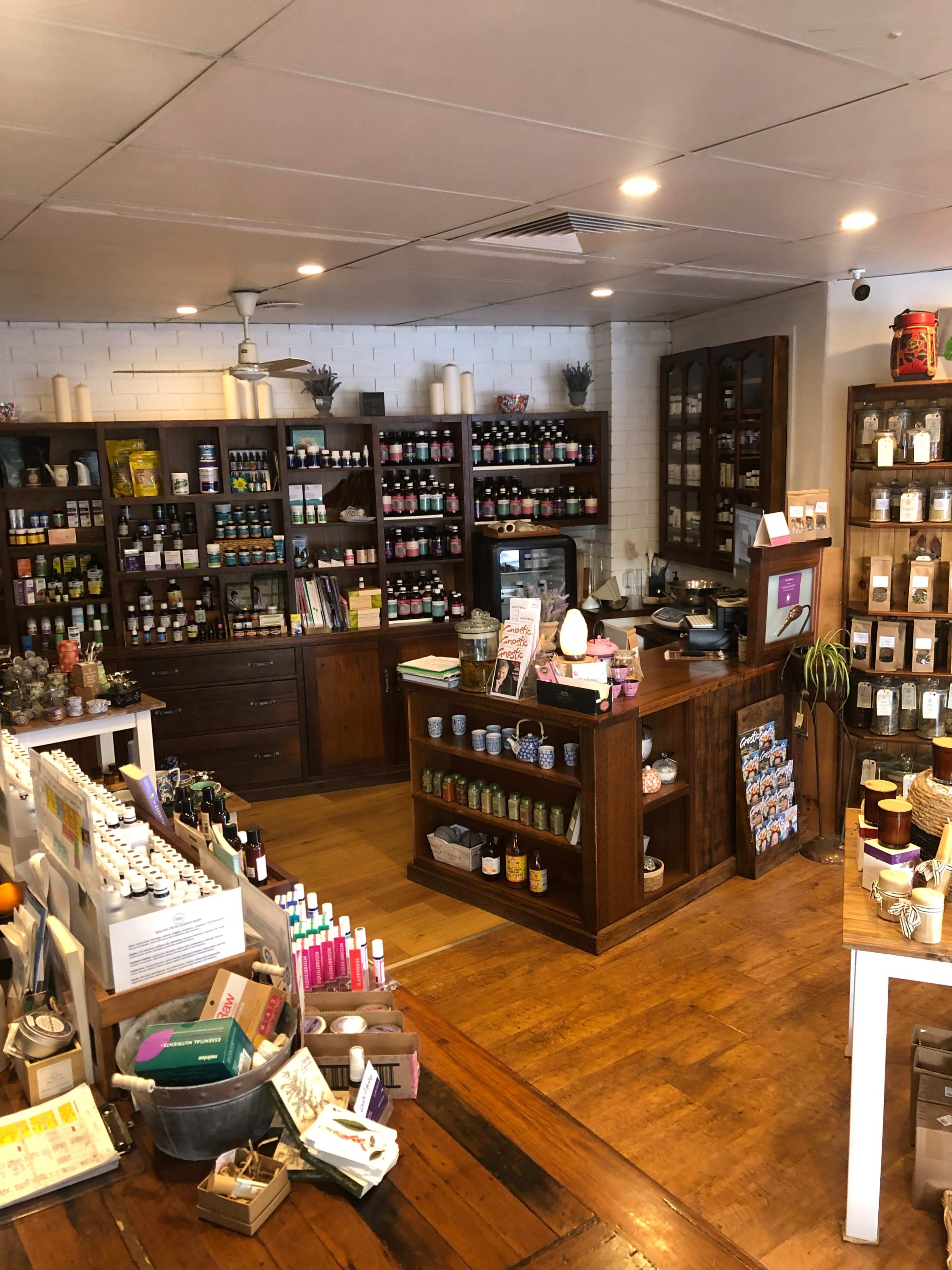 The image shows a well-organized shop interior featuring wooden shelves stocked with various bottles and jars of products, a counter at the front, and a warm wooden floor.