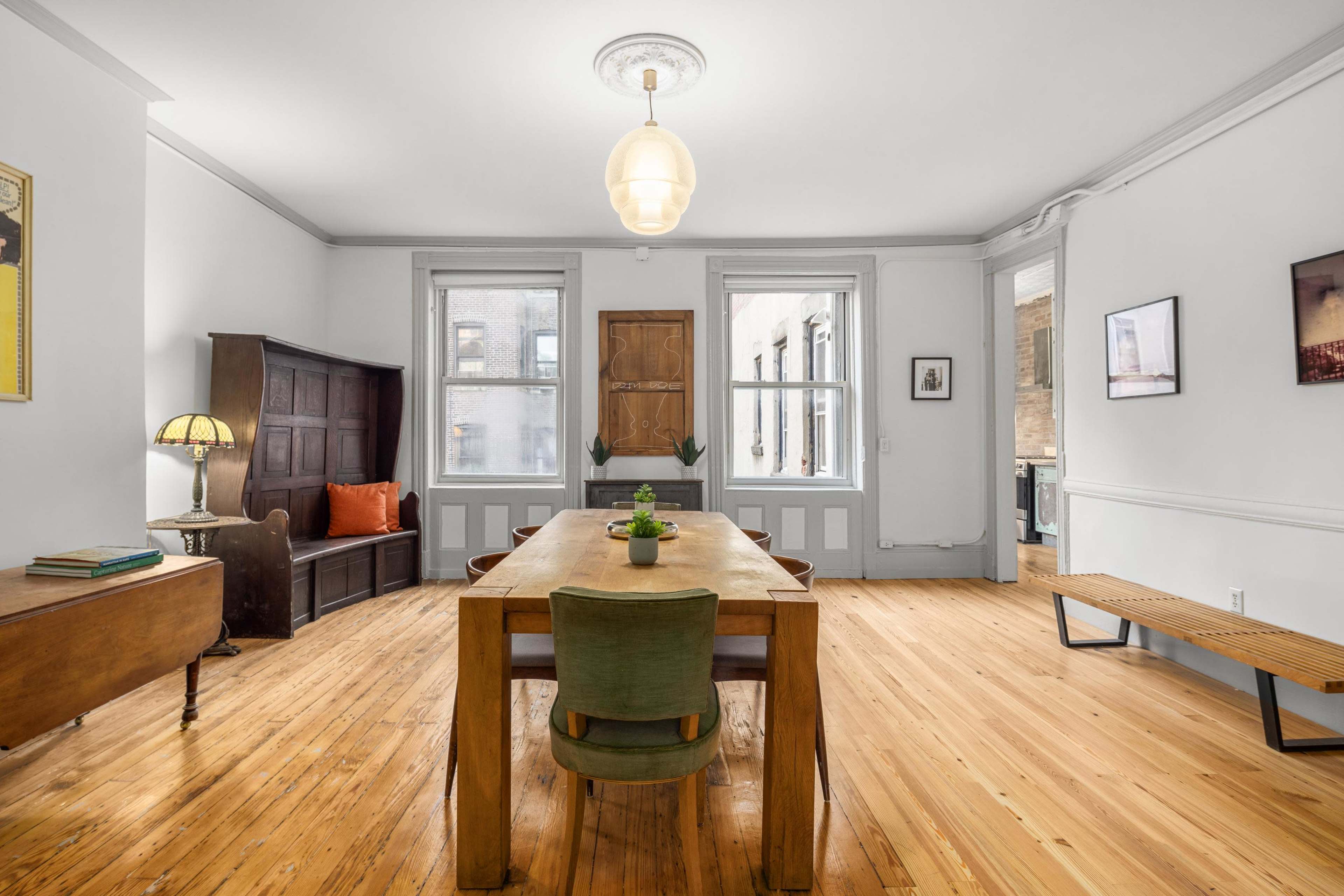 A well-lit dining area with a wooden table, green chair, and a hardwood floor, accompanied by a wooden bench and a few decorative items on the walls.
