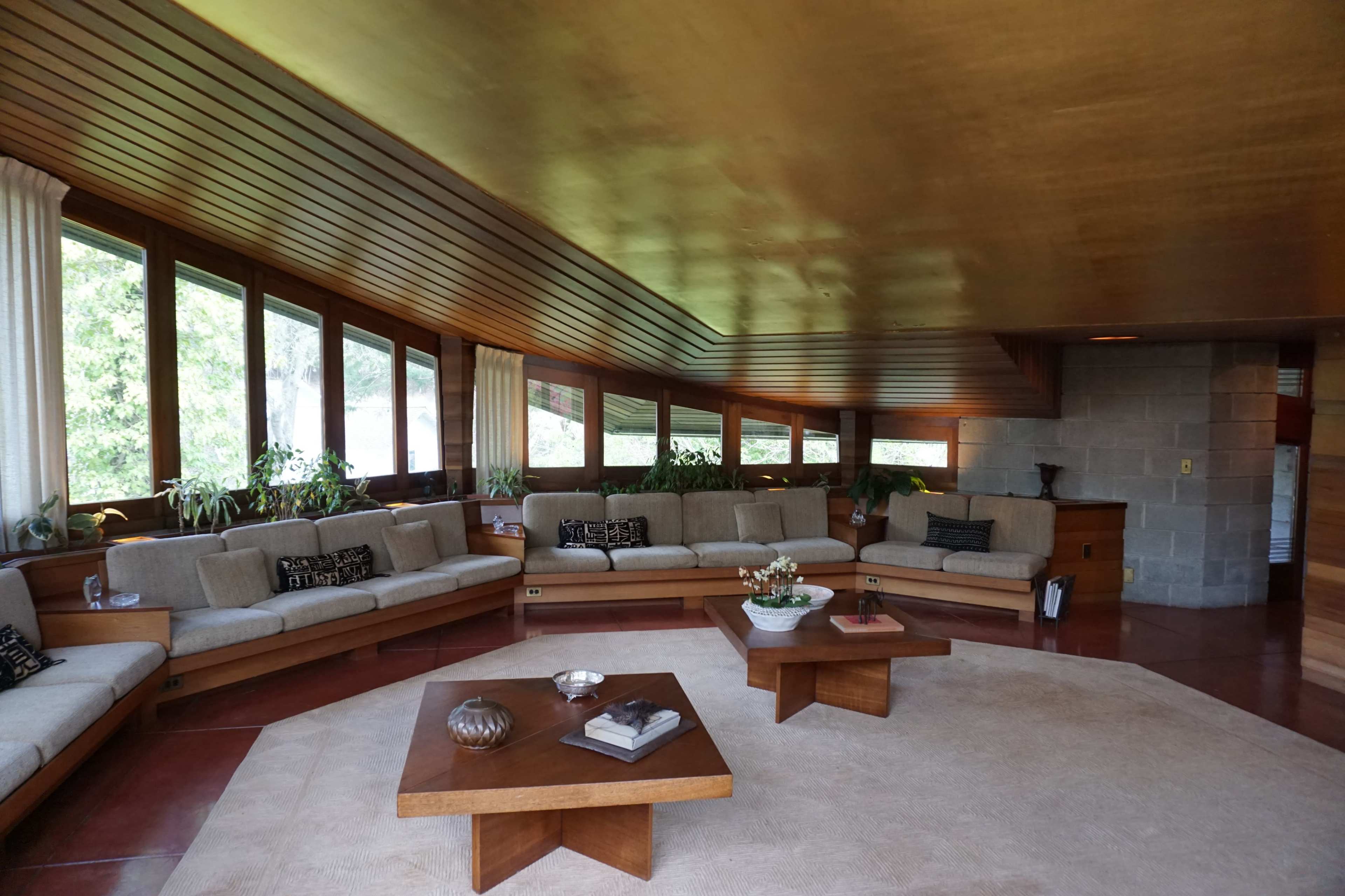 A spacious living room with a gold ceiling, large windows, and two wooden coffee tables surrounded by a sectional sofa.
