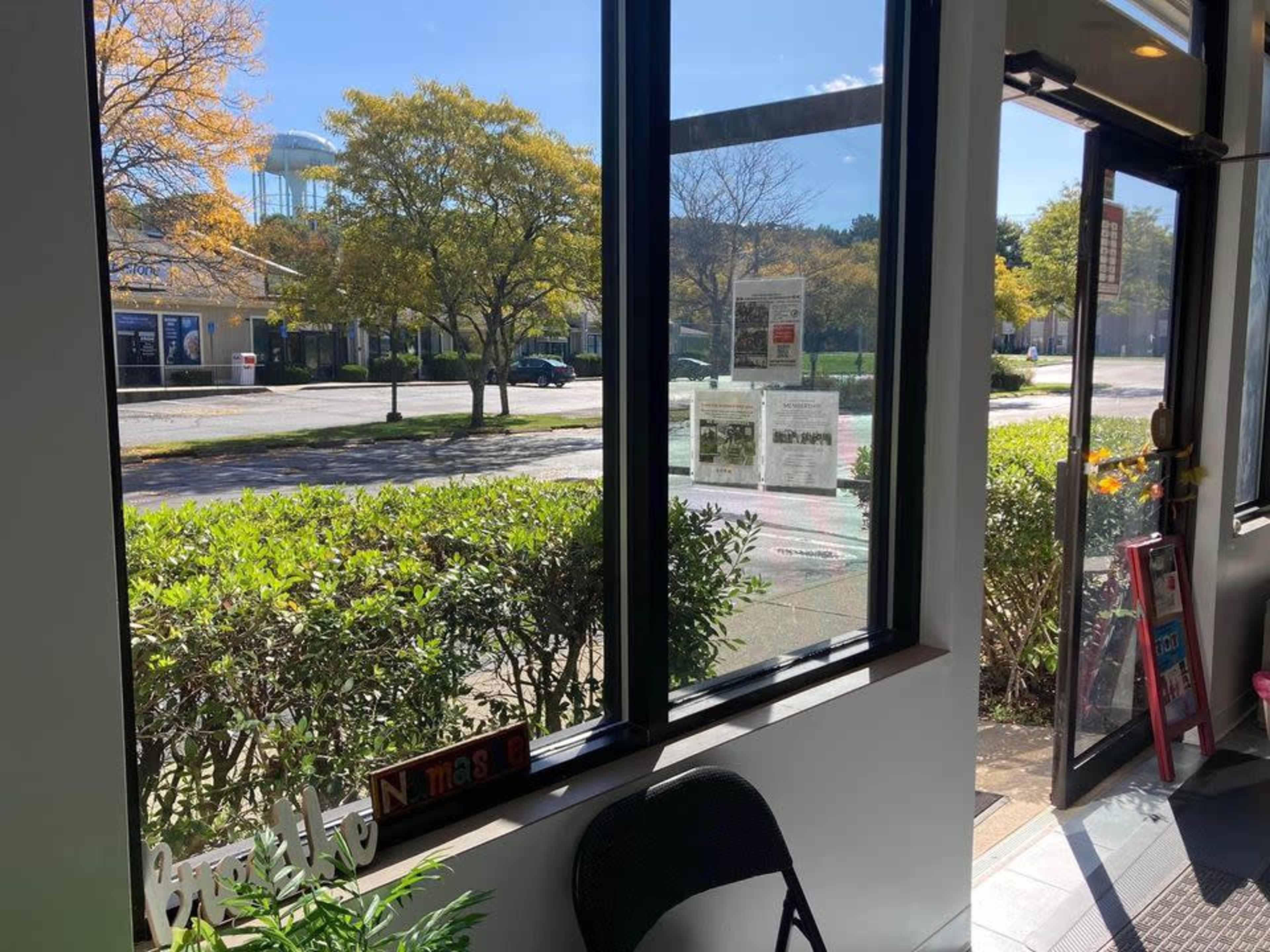 A view from inside a building looking out through large windows at a tree-lined street and parked cars.
