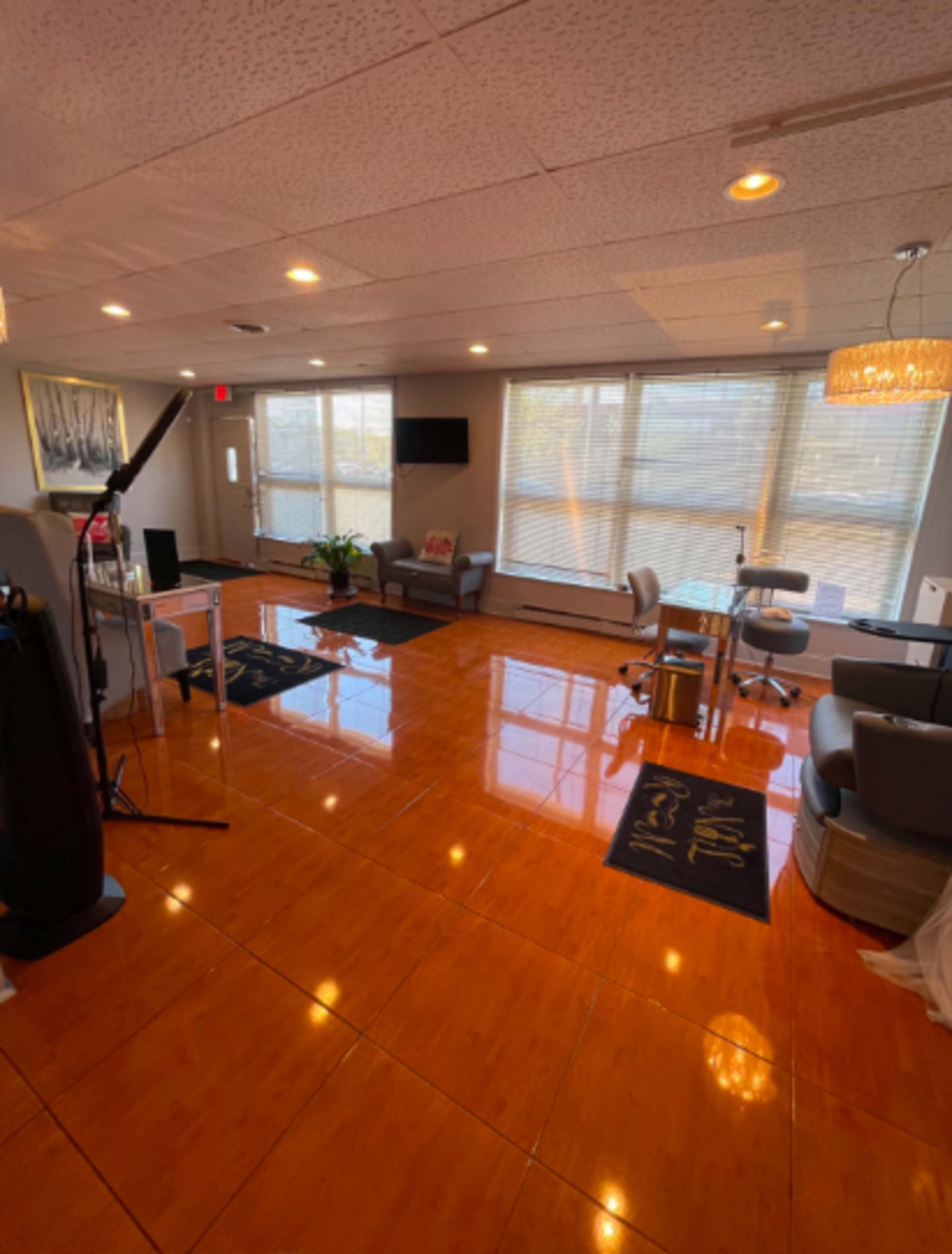 The image shows a well-lit, modern room featuring polished flooring, chairs, and a small meeting area with a large window.