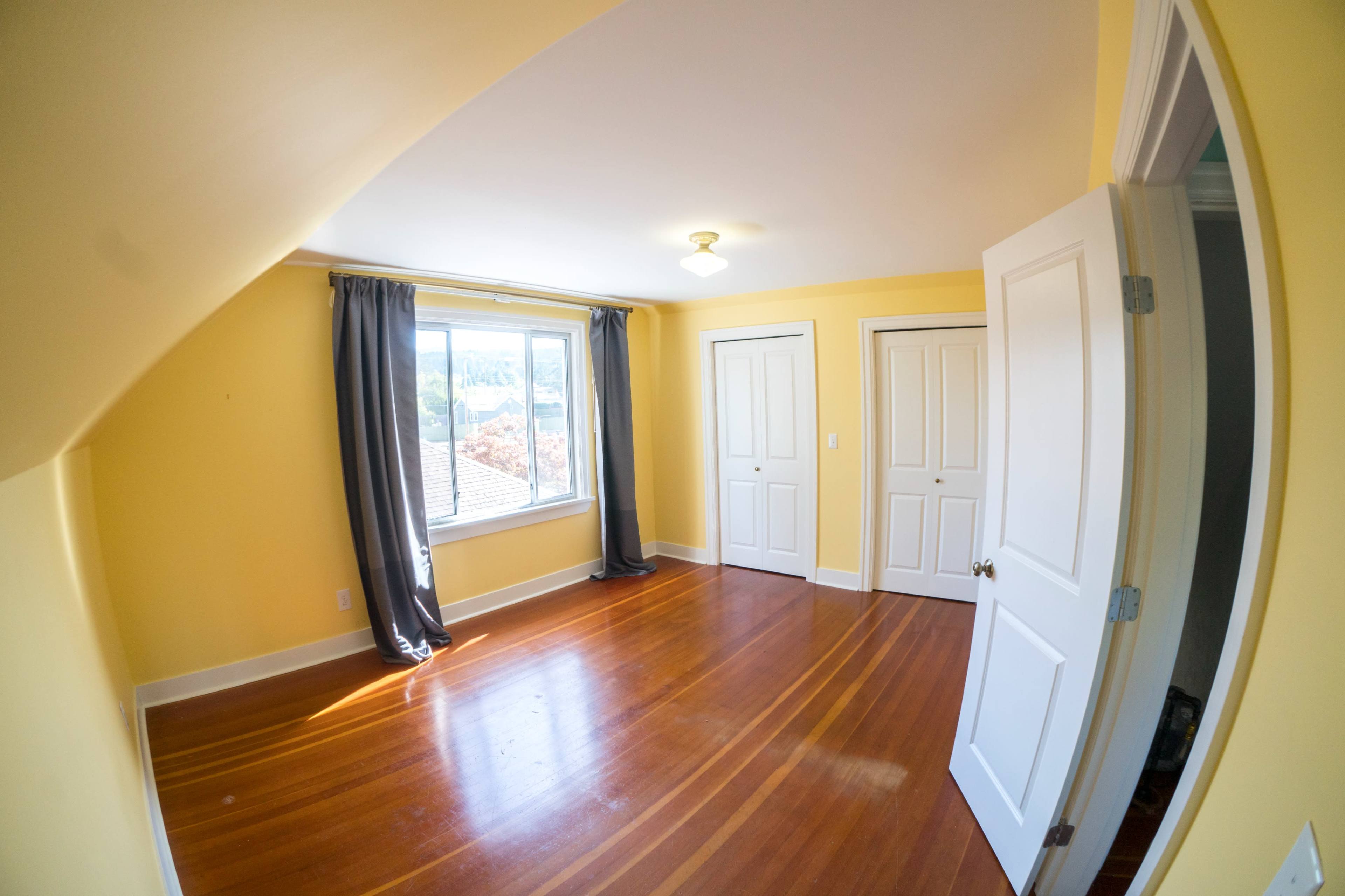 A yellow-walled room with wooden floors, two closed doors, and a window with gray curtains.