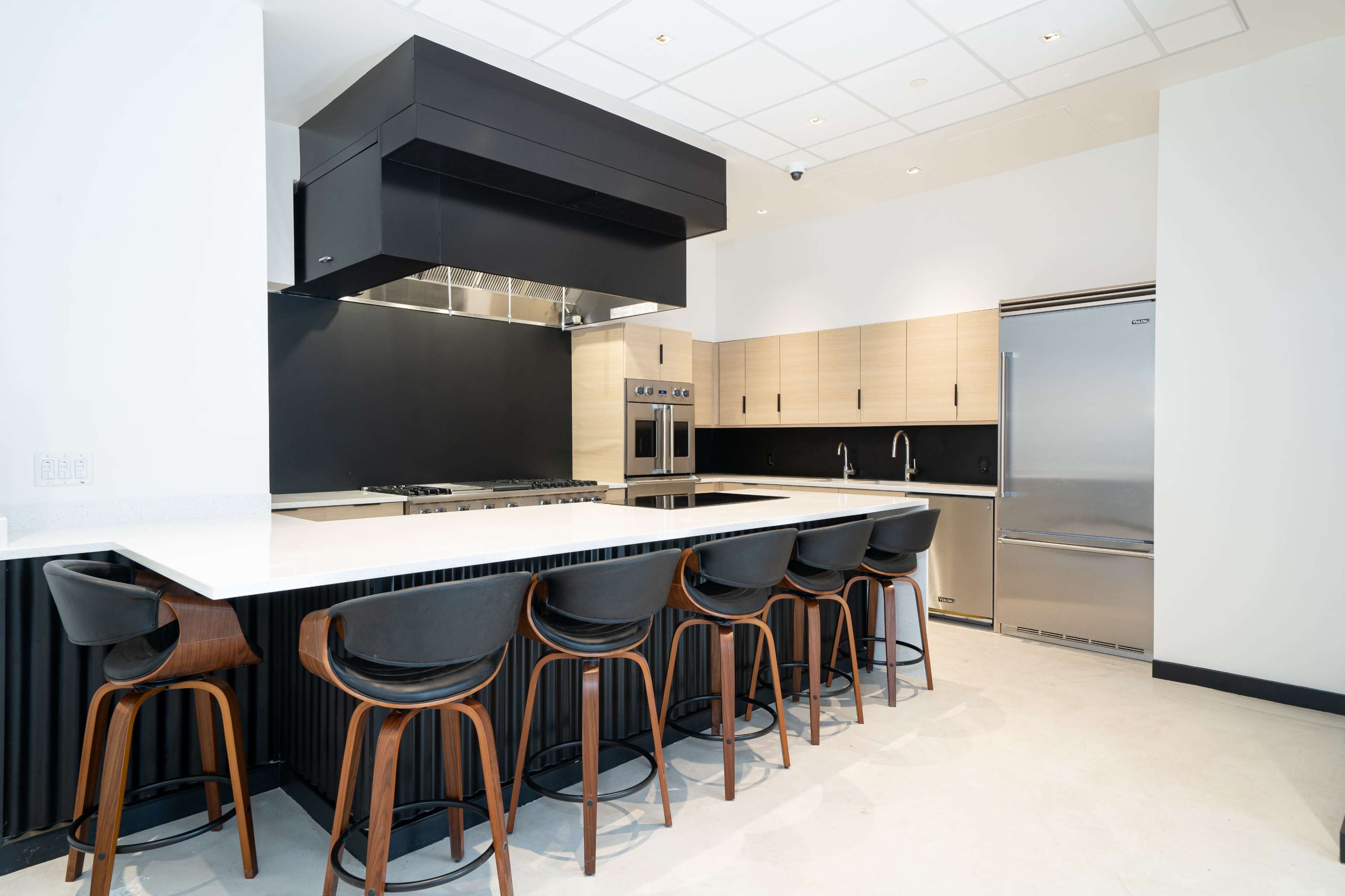 A modern kitchen with a black and wooden color scheme, featuring a large island with seating and stainless steel appliances.
