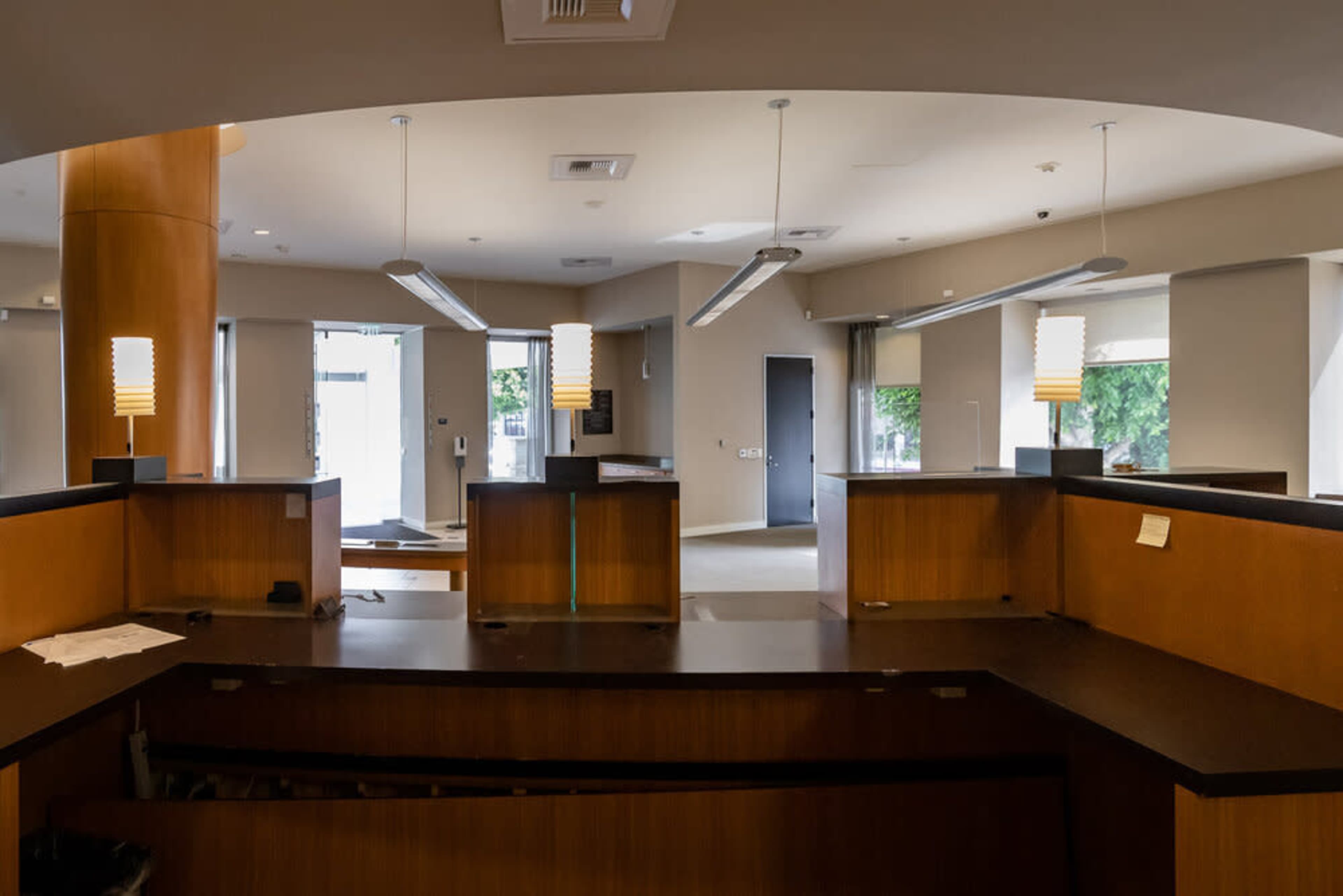 An empty reception area with wooden counters, pendant lighting, and large windows allowing natural light.