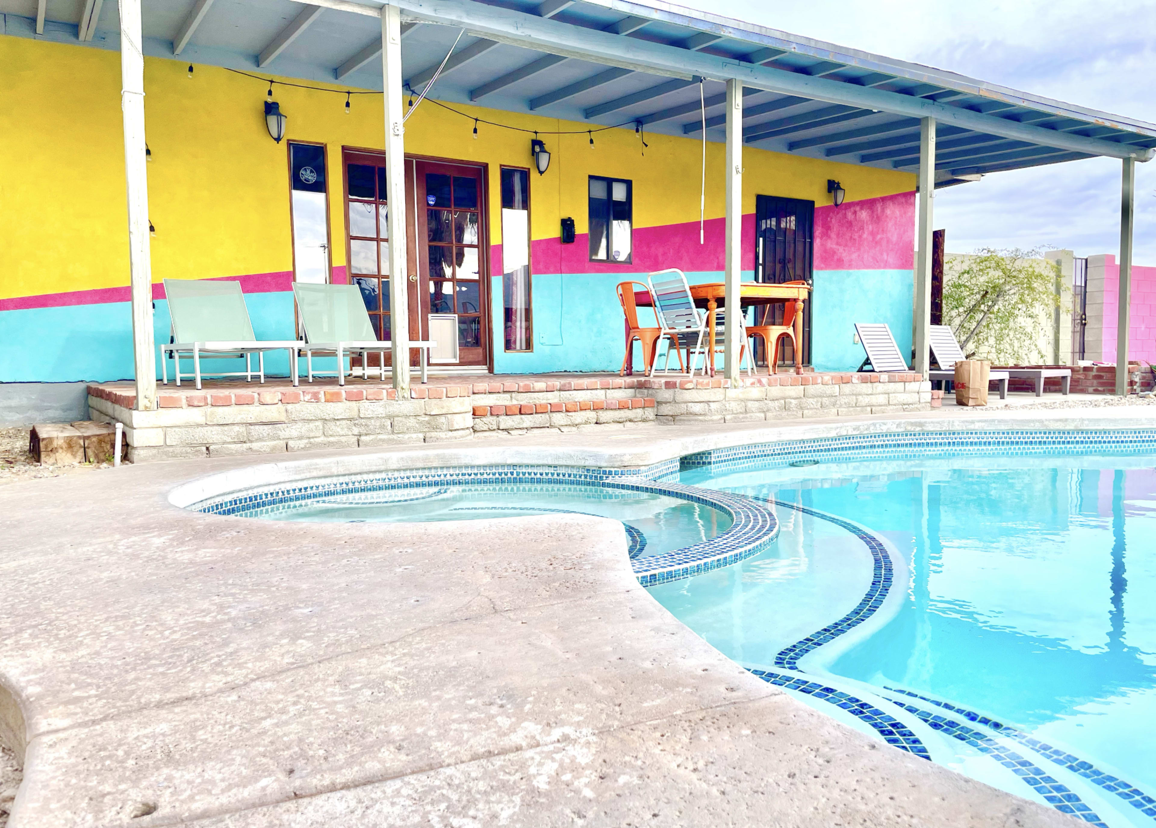 A colorful house with a pool features a yellow, pink, and blue exterior, and has seating by the water.