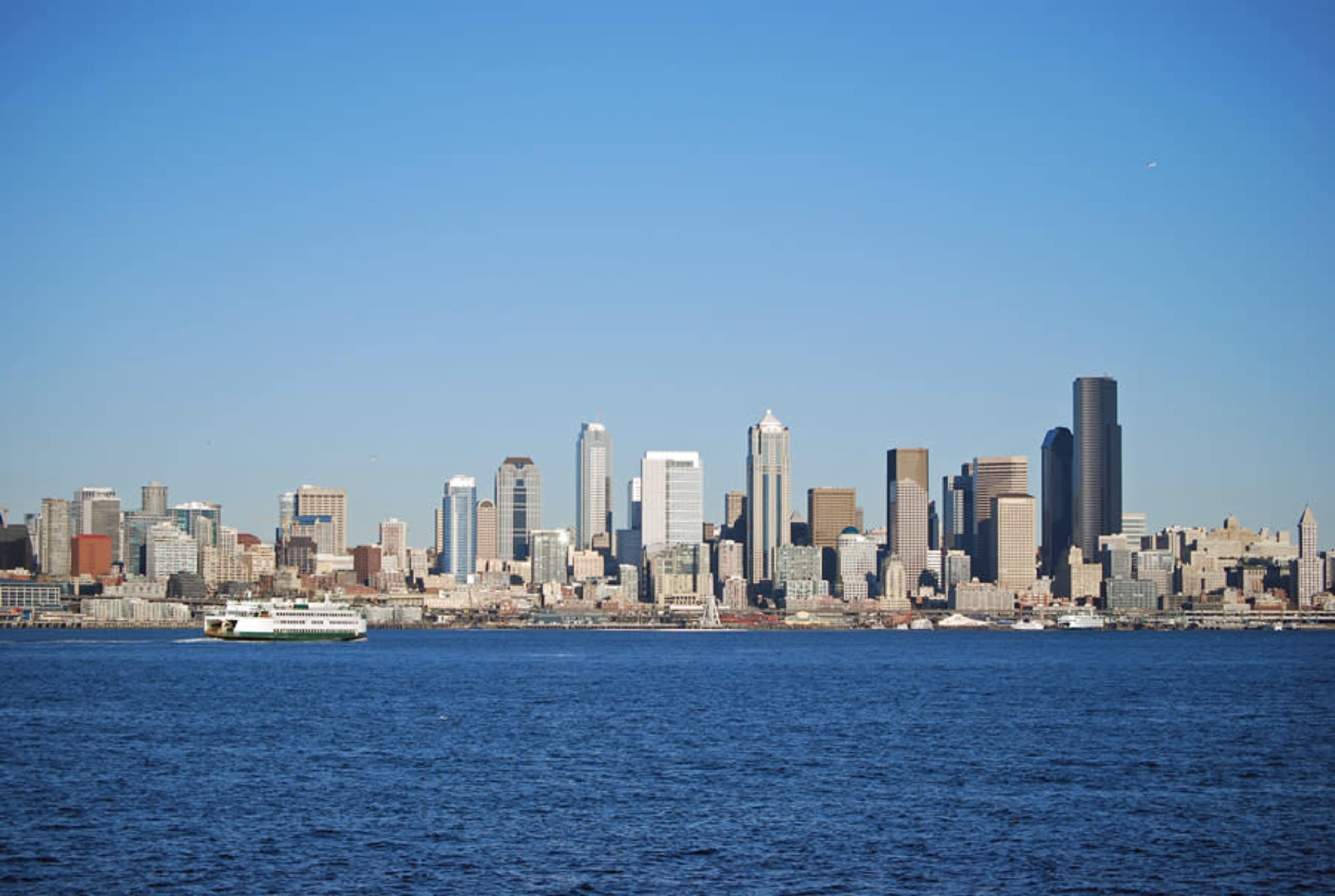 A skyline of tall buildings along a waterfront with a ferry in the foreground.