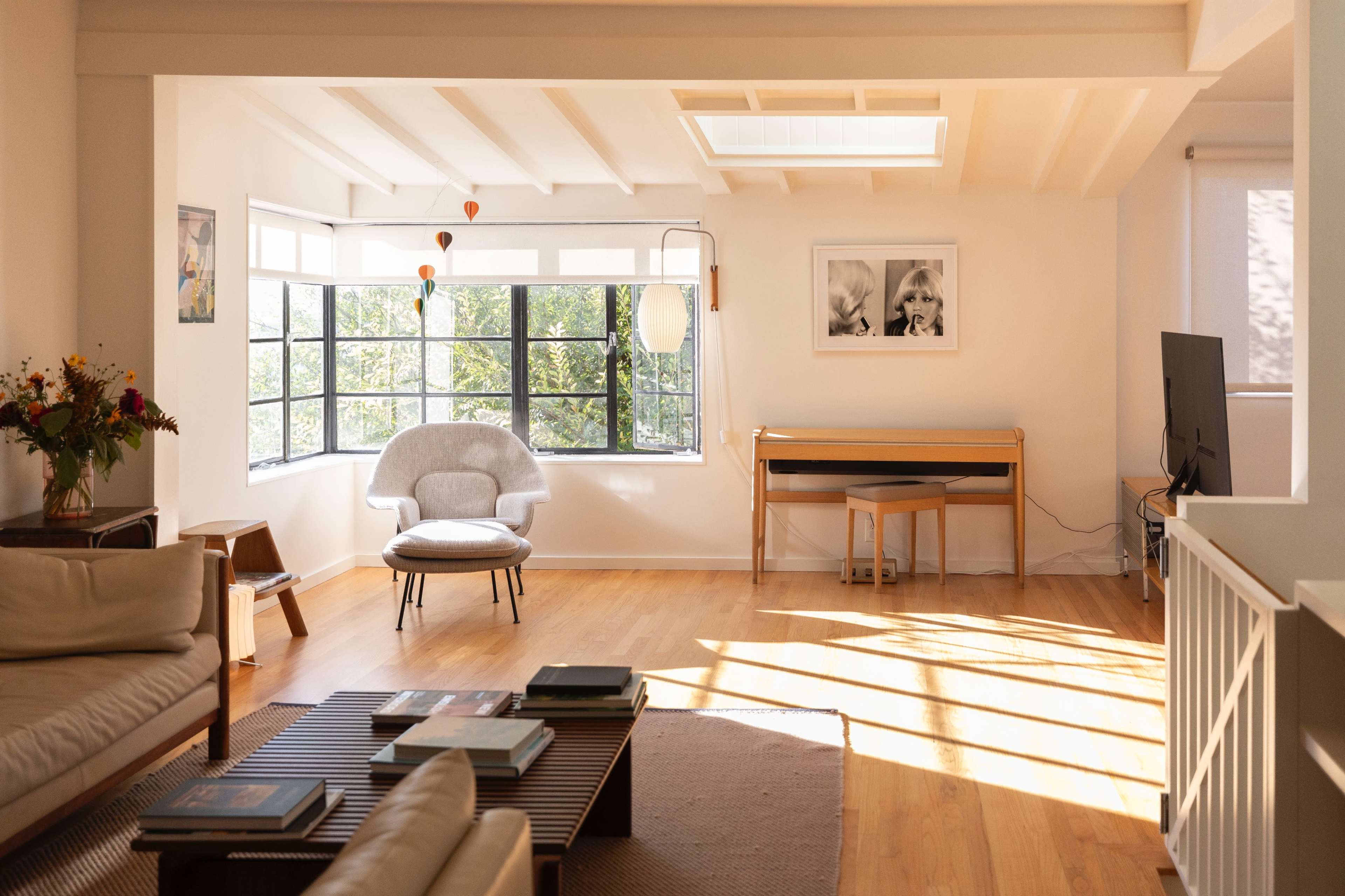 The image shows a spacious living room with a large window, a cozy armchair, a wooden table, and a television.