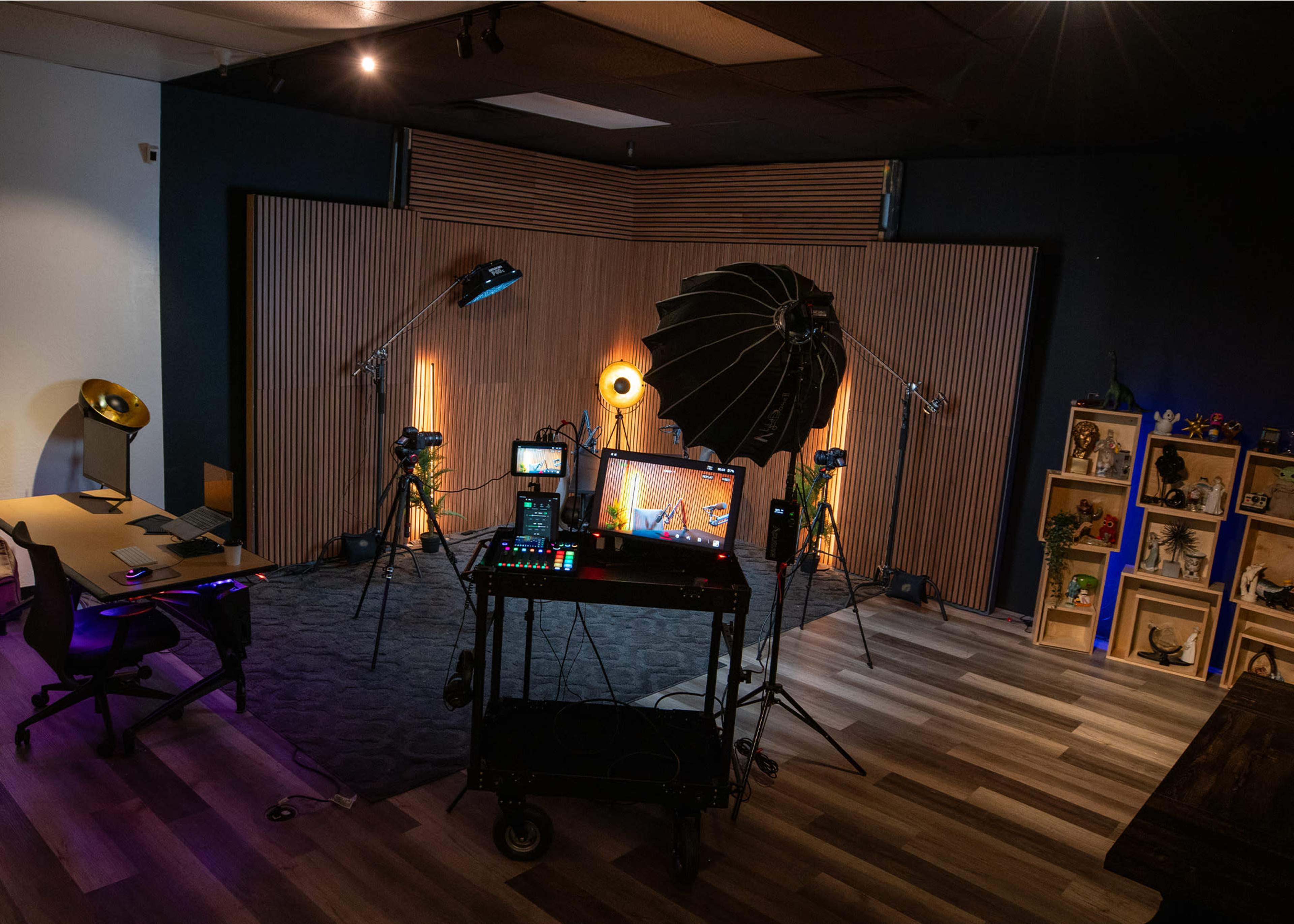 The image shows a well-equipped studio with multiple cameras, lighting setup, and a desk, arranged for a video production.