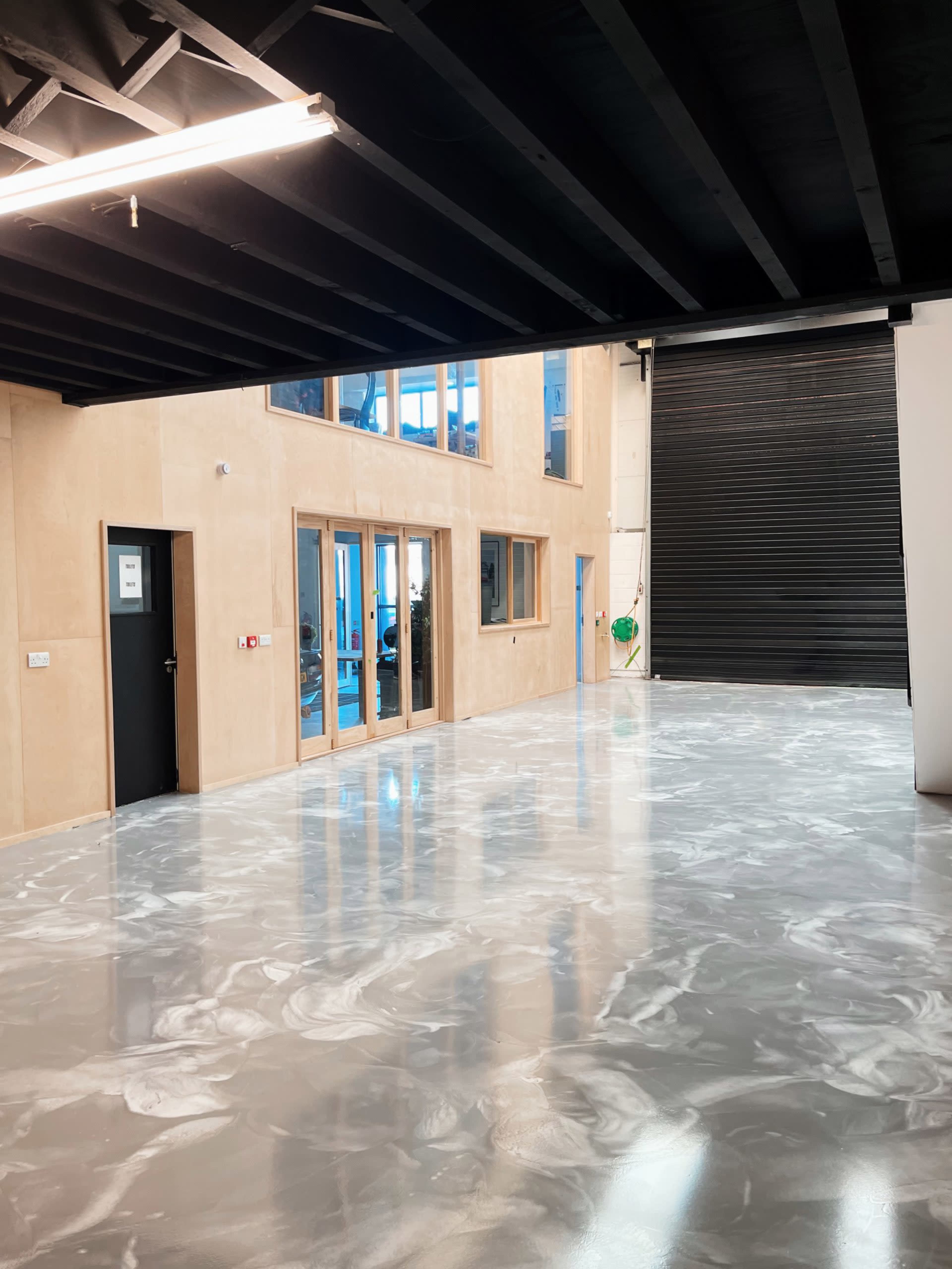An industrial-style interior space with a glossy marbled floor, large windows, and a roll-up door.