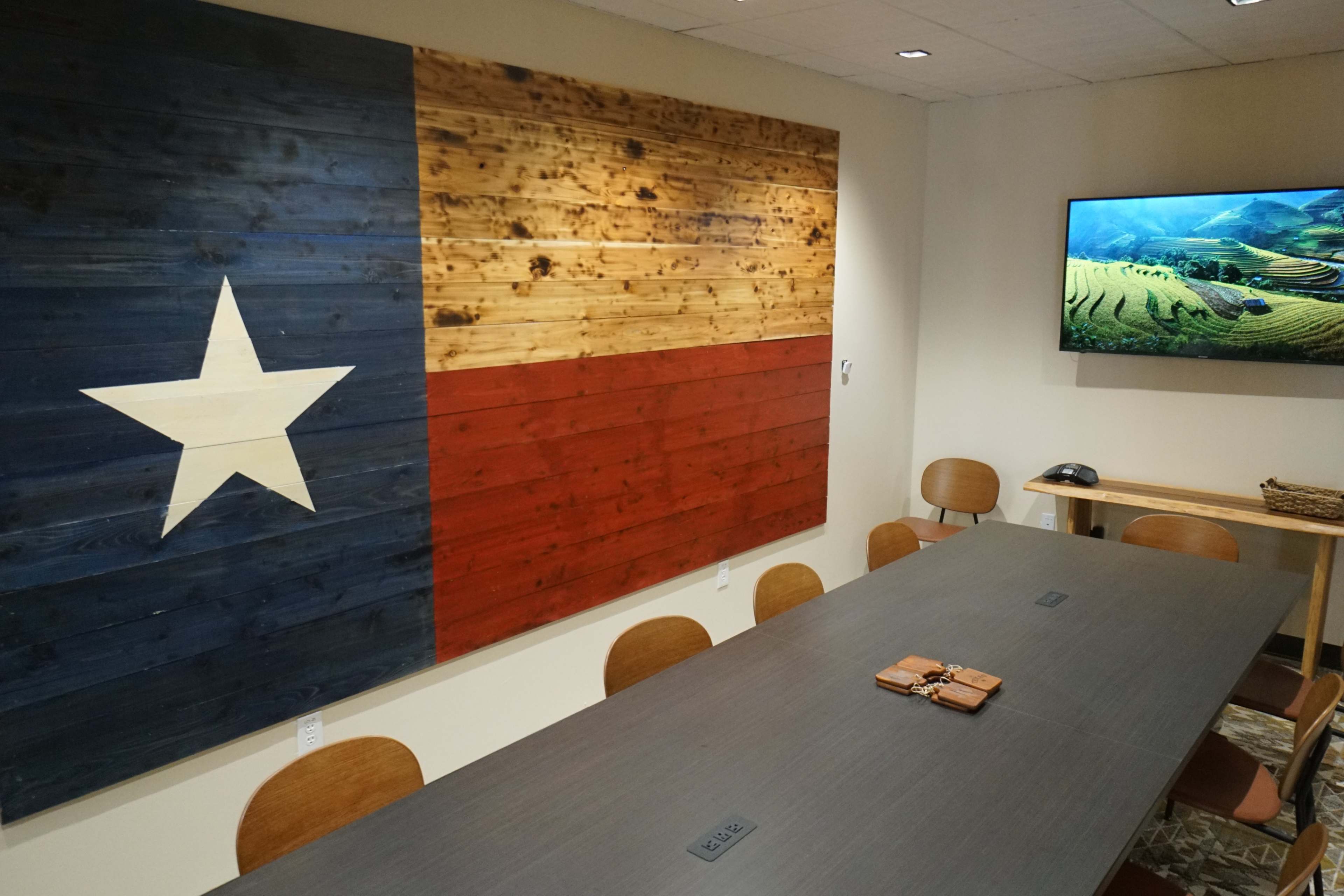 A conference room with a wooden wall displaying a Texas flag and a large table surrounded by chairs.