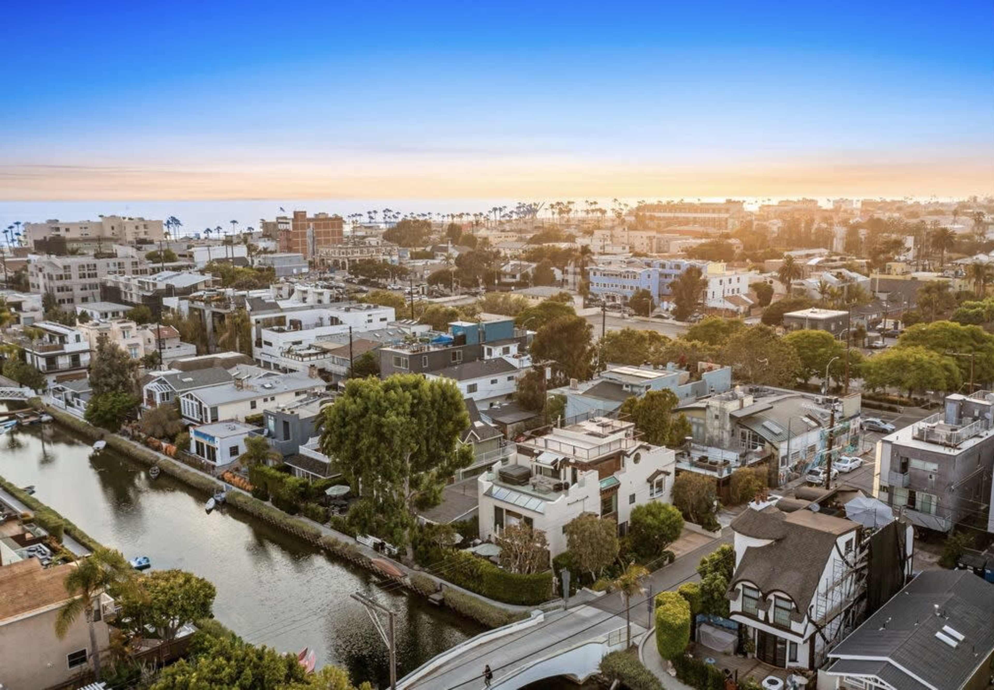 A coastal urban area with a network of canals, lined by residential buildings and palm trees under a sunset sky.