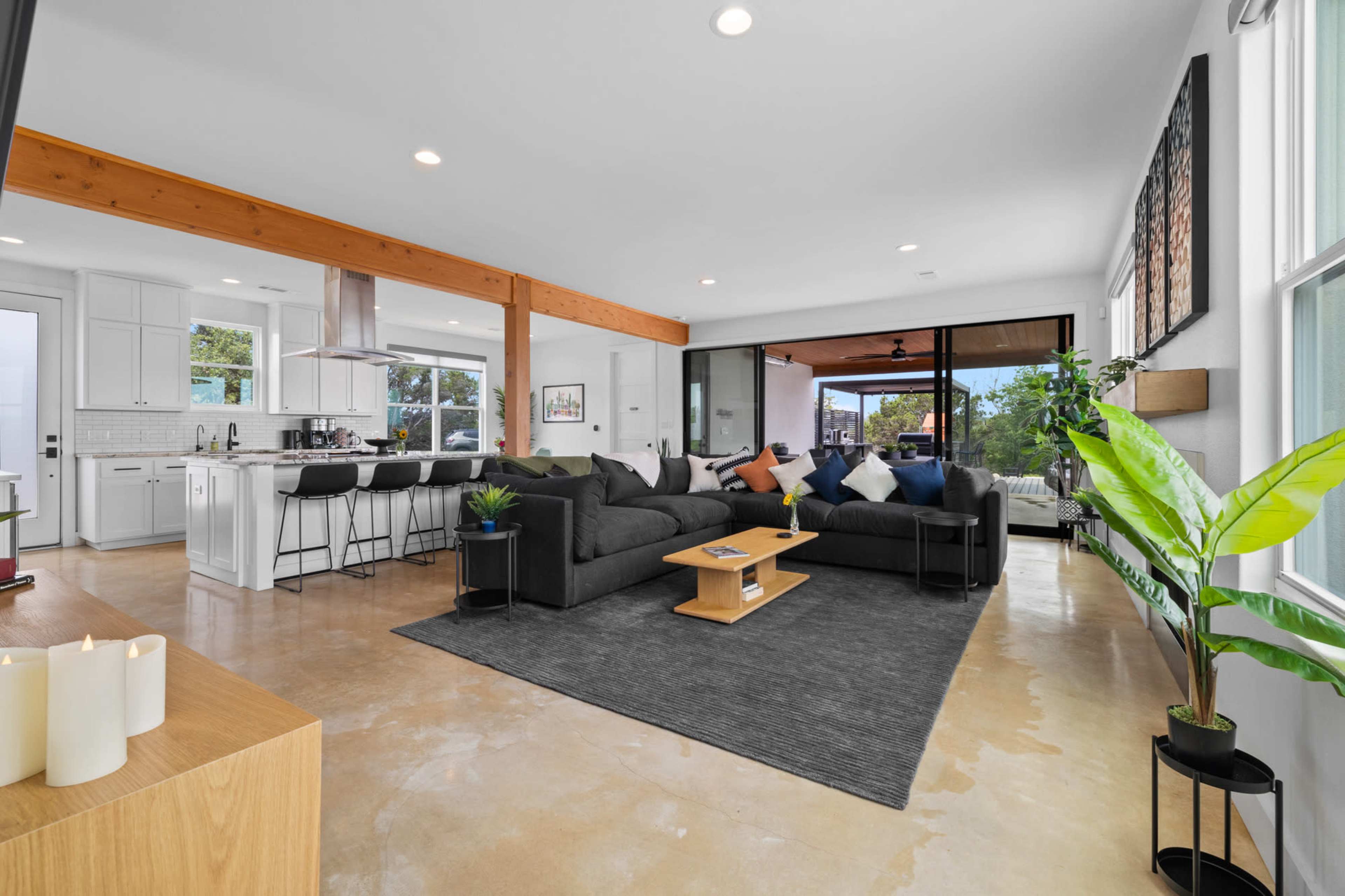 A spacious living room features a gray sectional sofa, a light wood coffee table, and large windows that open to an outdoor patio.