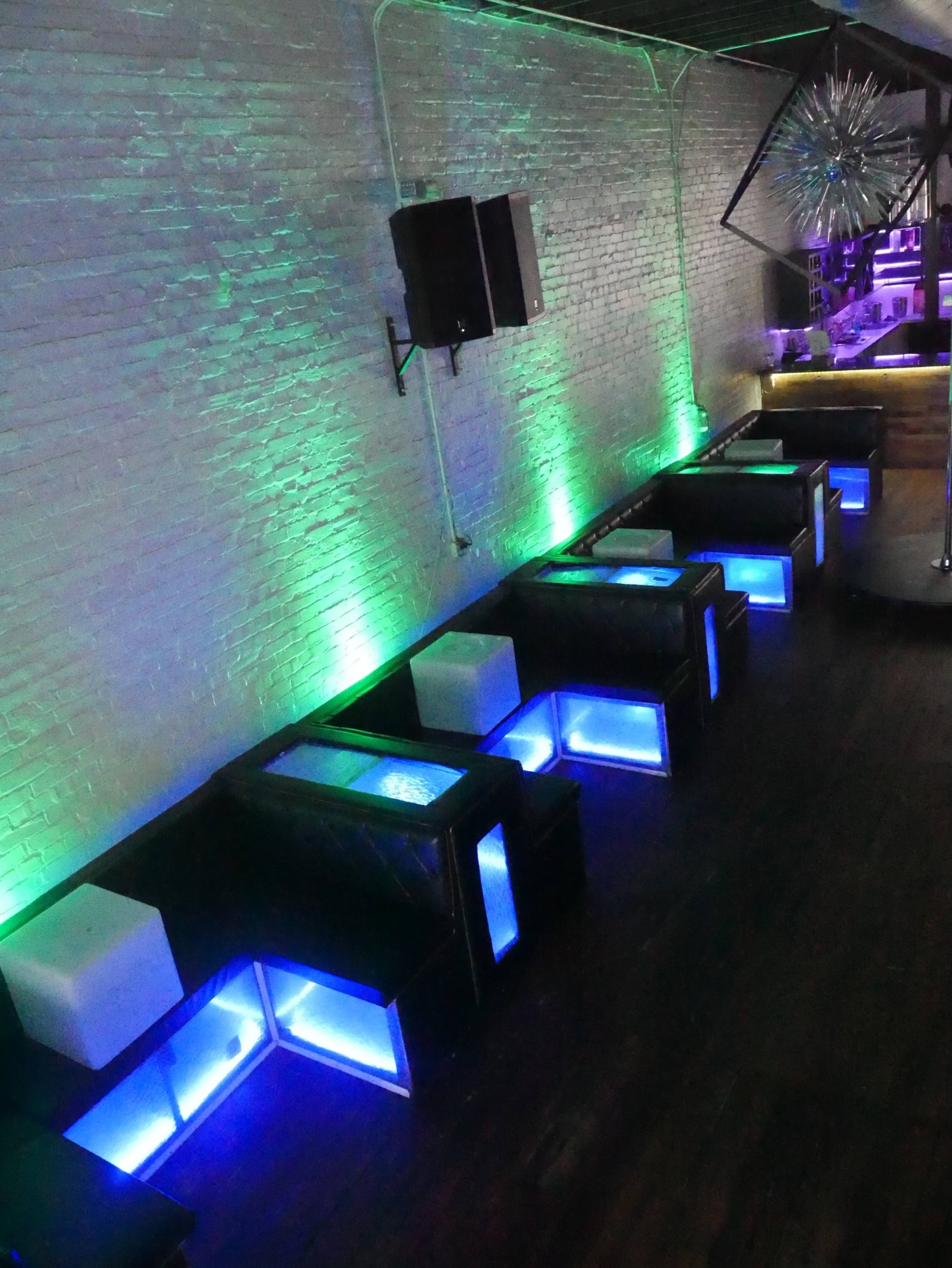 A dimly lit lounge with illuminated seating areas featuring blue LED lights along the edges.