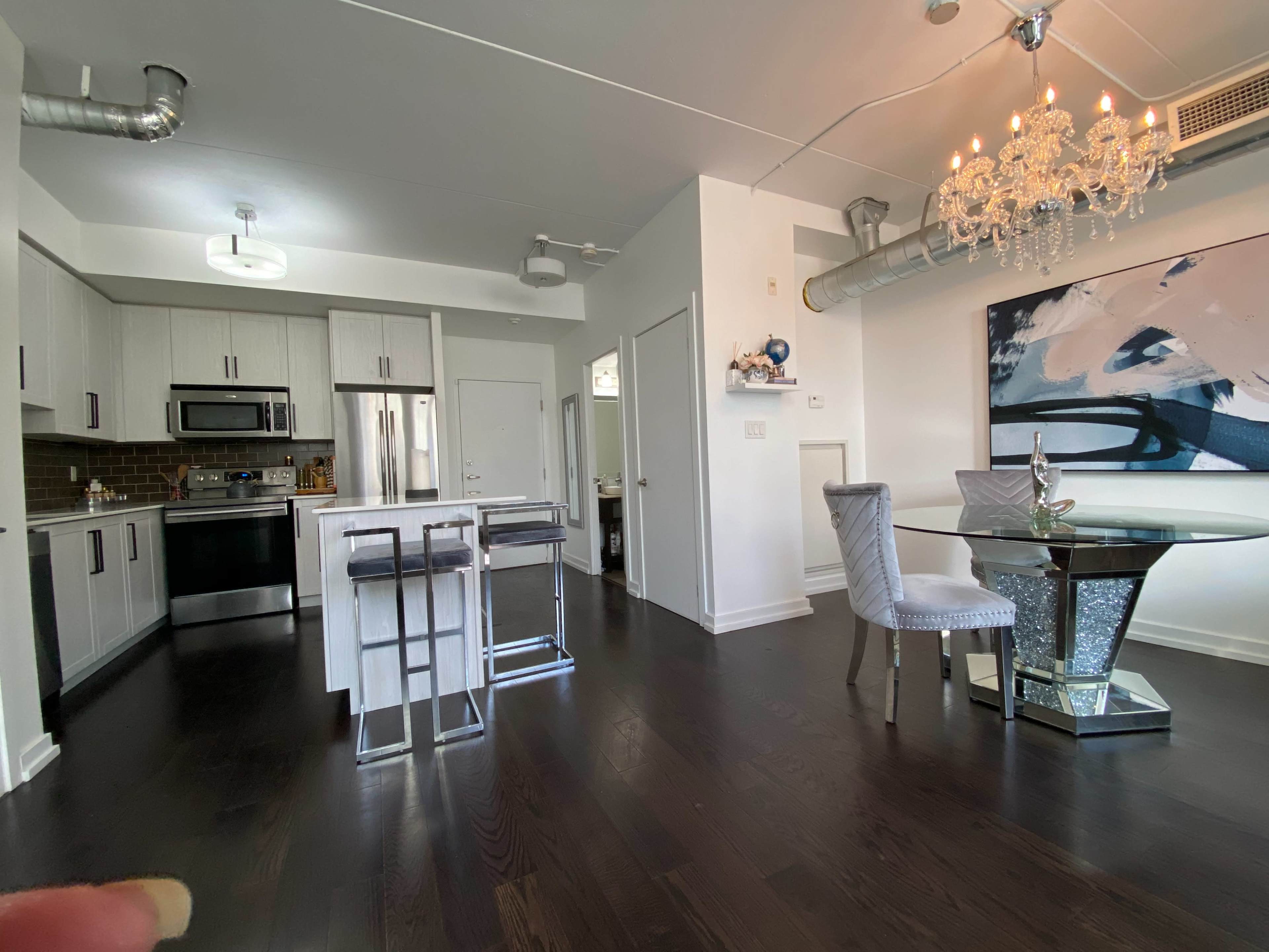 The image shows a modern, open-concept kitchen and dining area featuring stainless steel appliances, a dining table with mirrored accents, and stylish chairs.