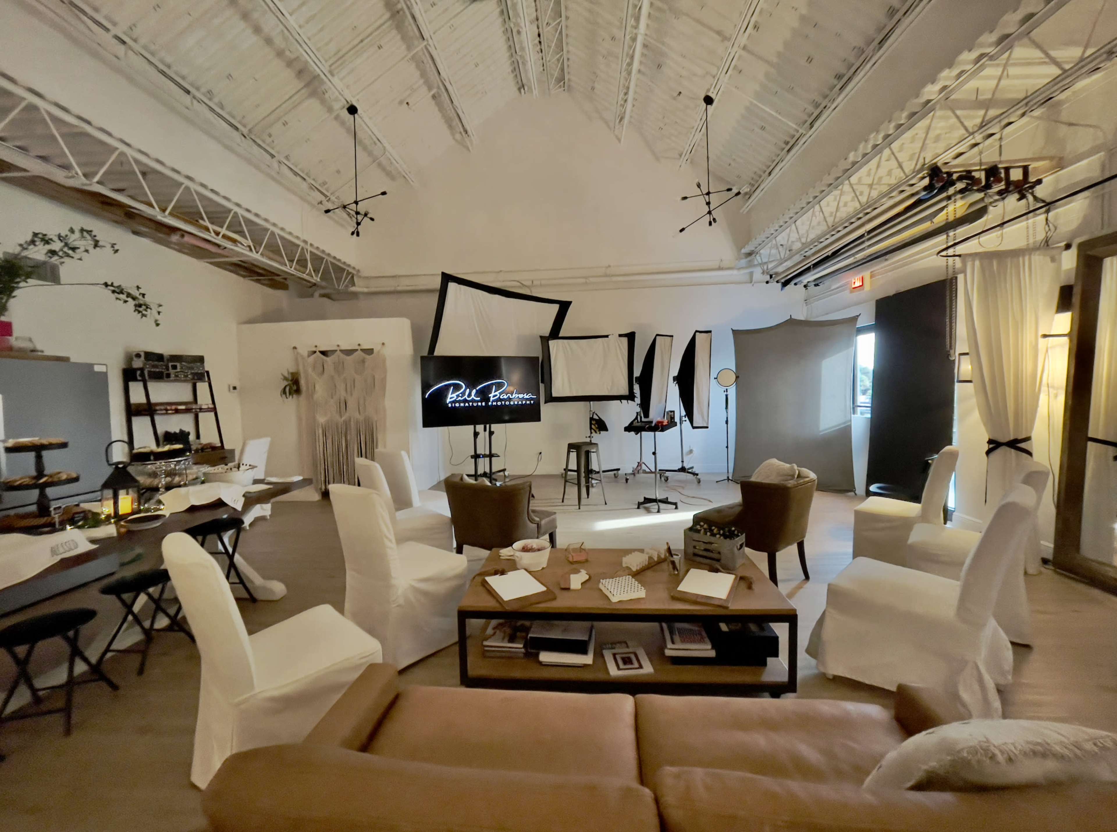 The image shows a modern studio space set up for a photo shoot, featuring a mix of chairs, a television screen, and various backdrops arranged around the room.