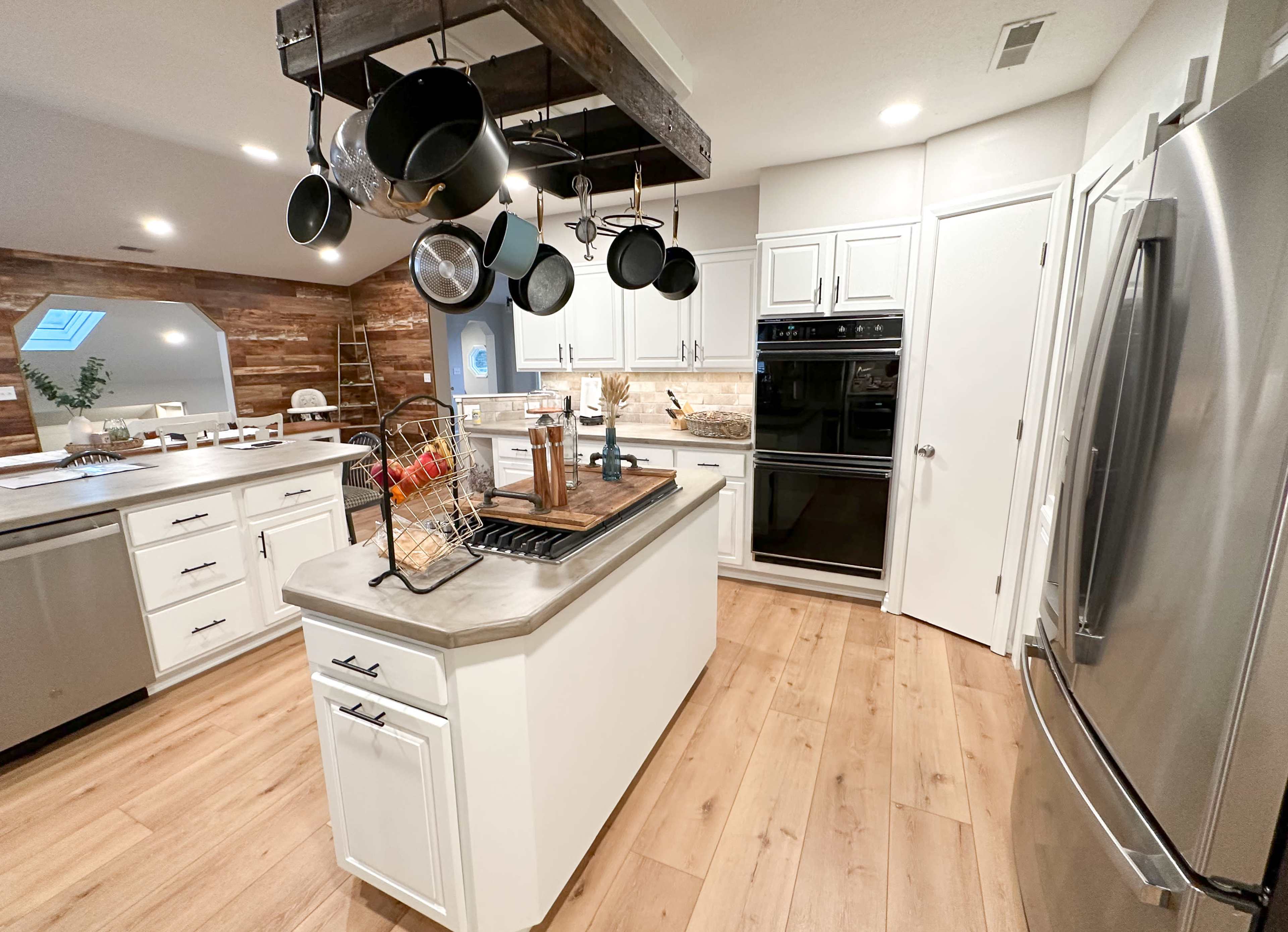 A modern kitchen with white cabinetry, a central island, and metal pots hanging from a wooden rack above.