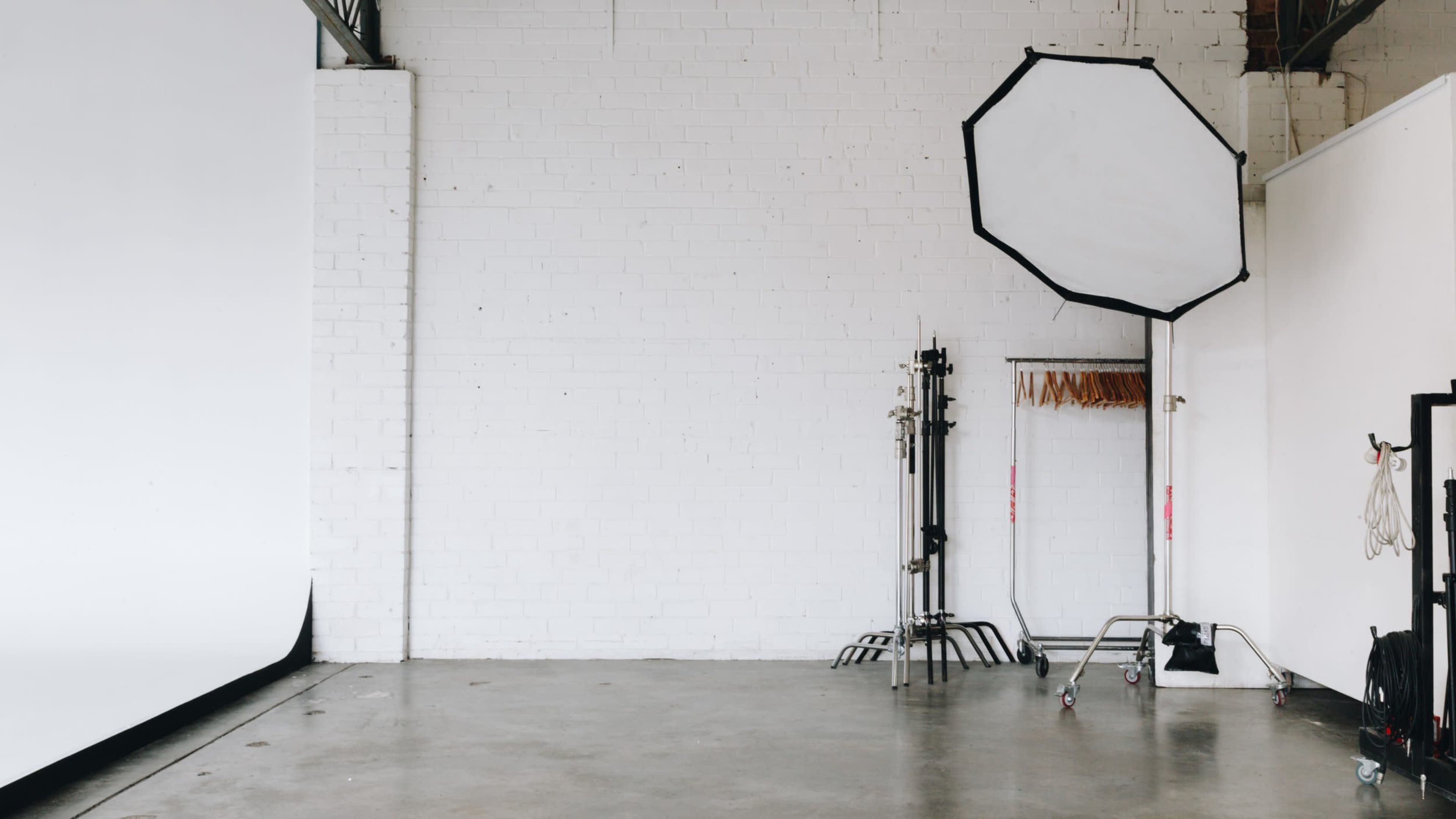 A photography studio with a blank wall, a large octagonal softbox on a stand, and a clothing rack against the wall.
