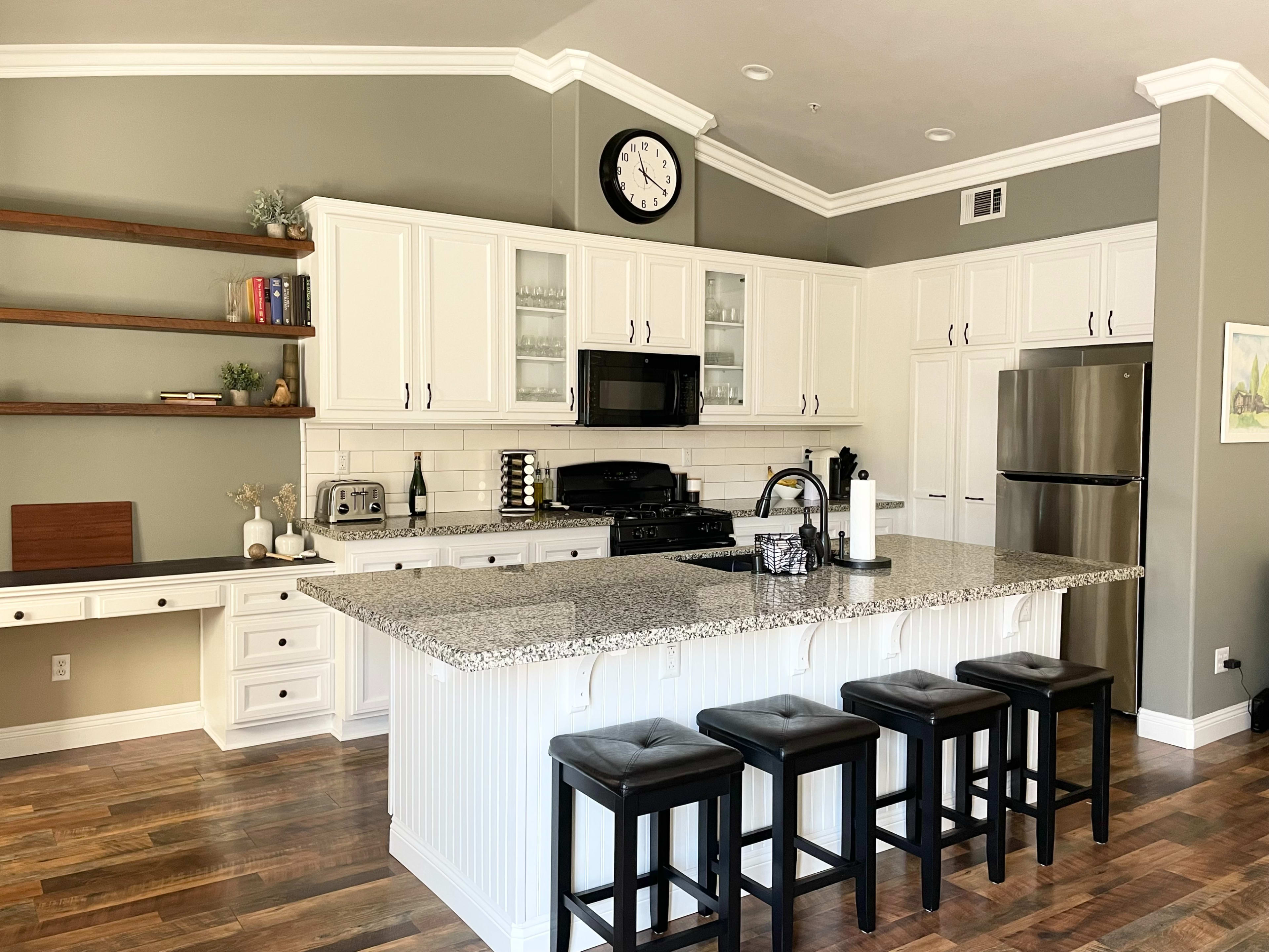 The image shows a modern kitchen with white cabinetry, a large island with seating, and stainless steel appliances.