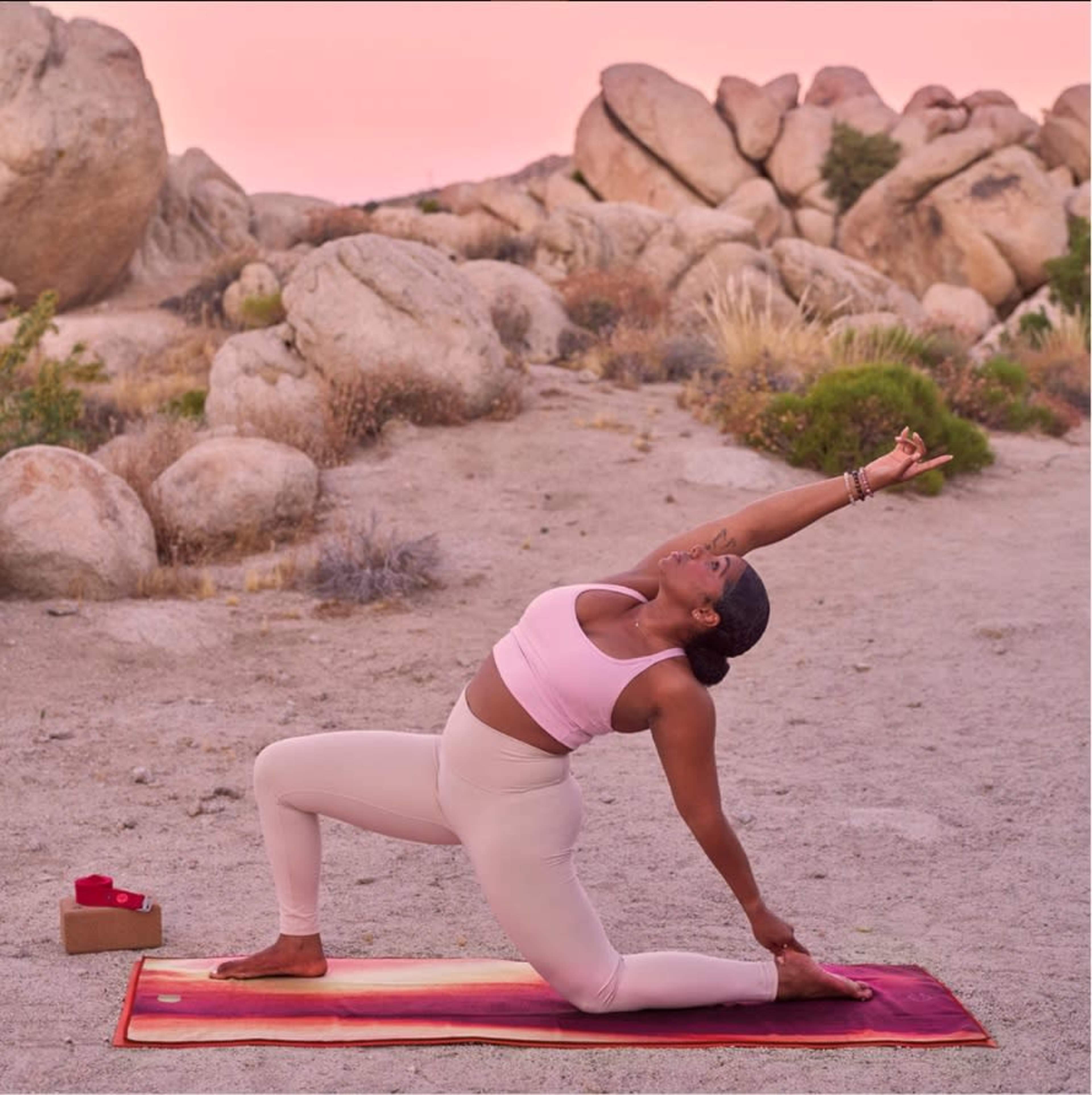 A person performs a yoga pose in a desert landscape surrounded by large boulders at sunset.