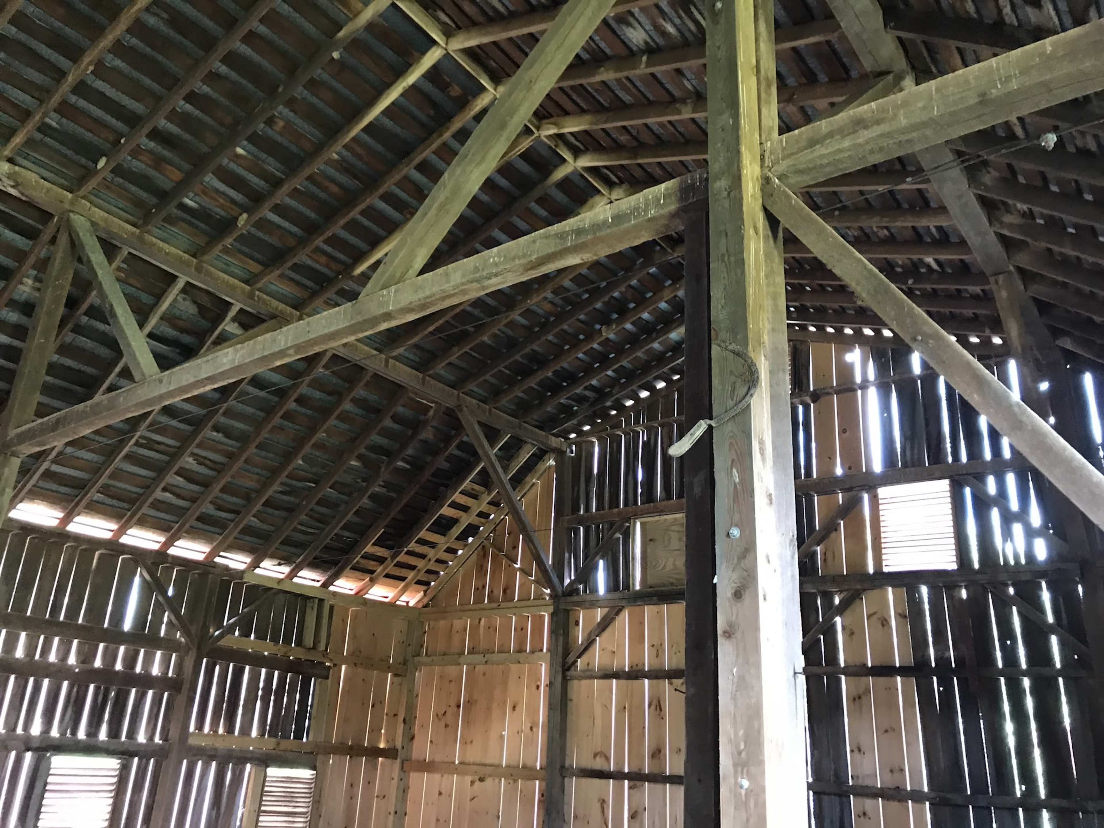 The interior of a wooden barn with exposed beams and walls, featuring gaps between the vertical wooden planks.