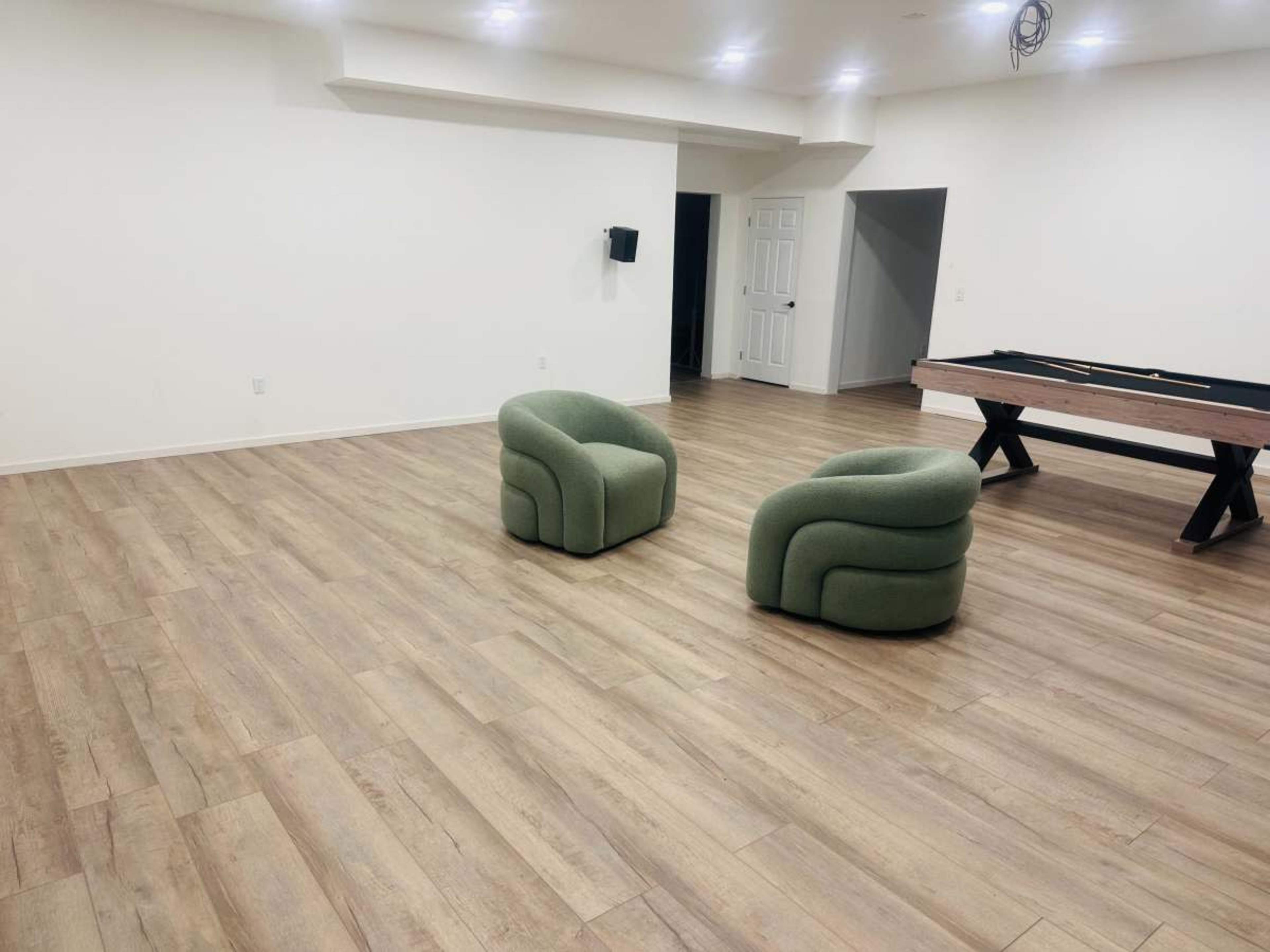 The image shows a spacious room with two green, curved armchairs facing each other and a pool table in the background.