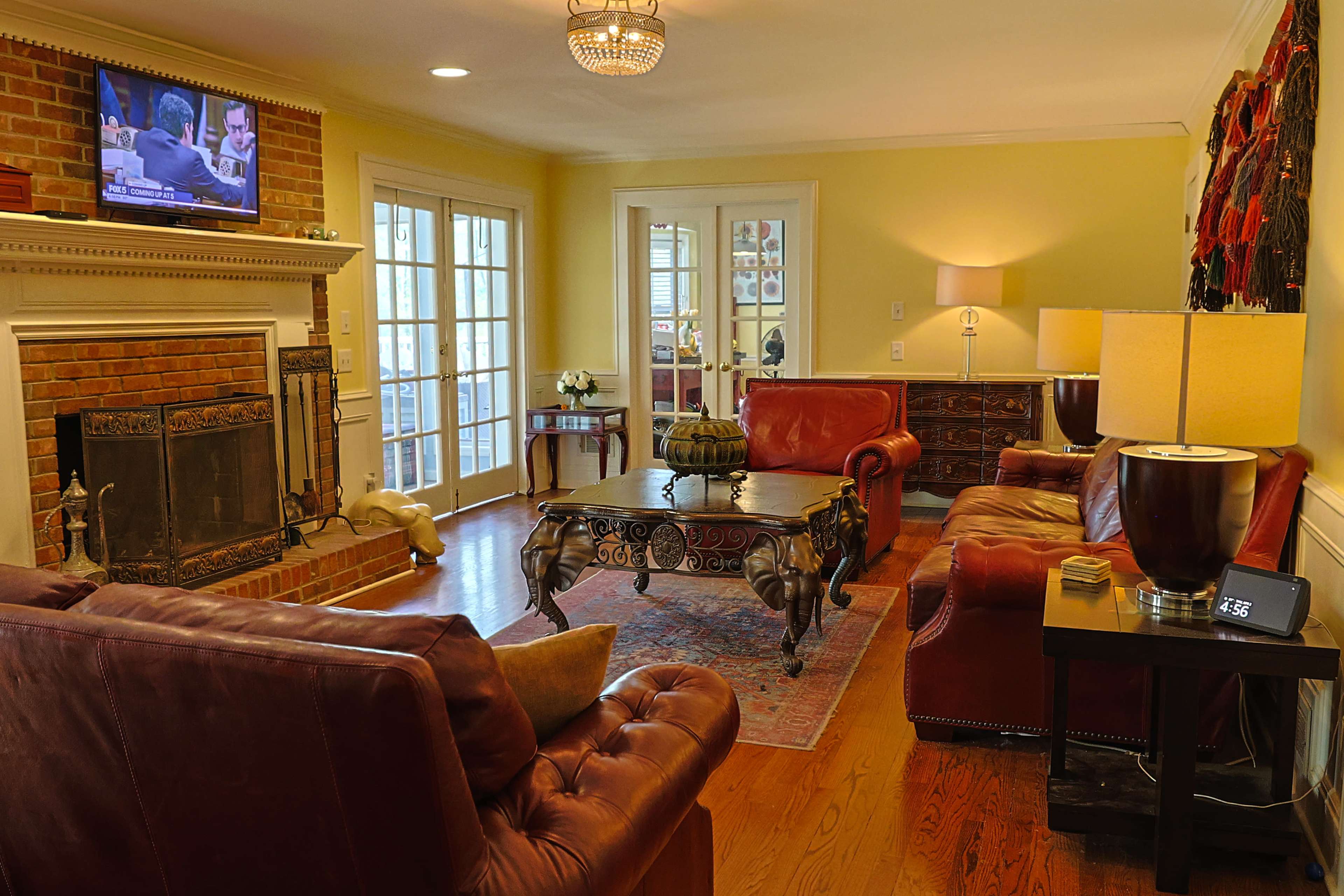 The living room features red leather sofas, a wooden coffee table, a brick fireplace, and a television mounted above the mantel.