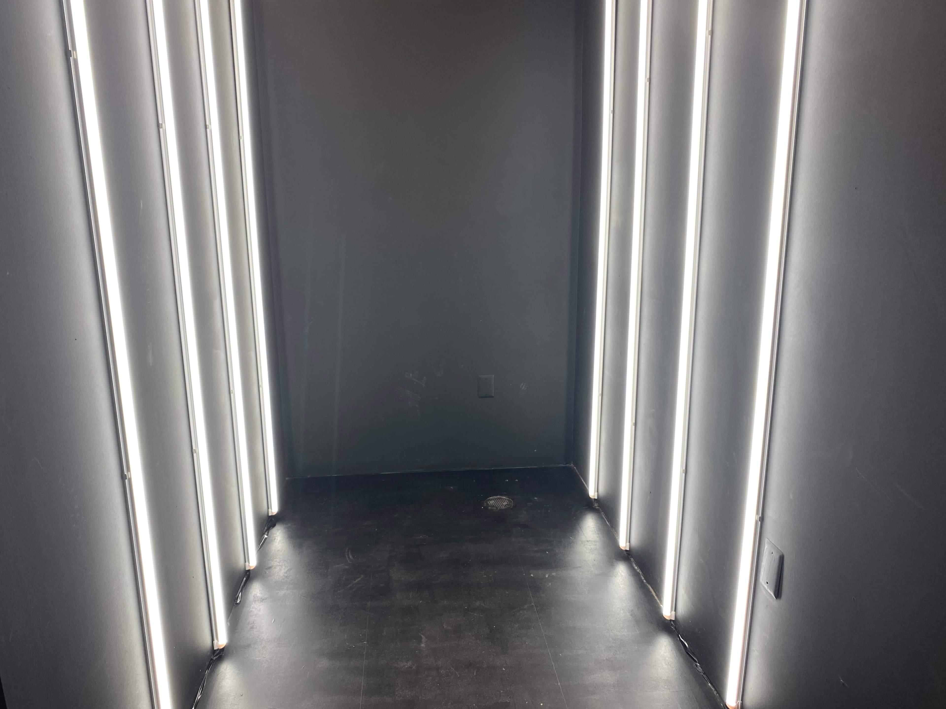 A dimly lit hallway with vertical fluorescent lights along the walls, leading to a darkened space at the end.
