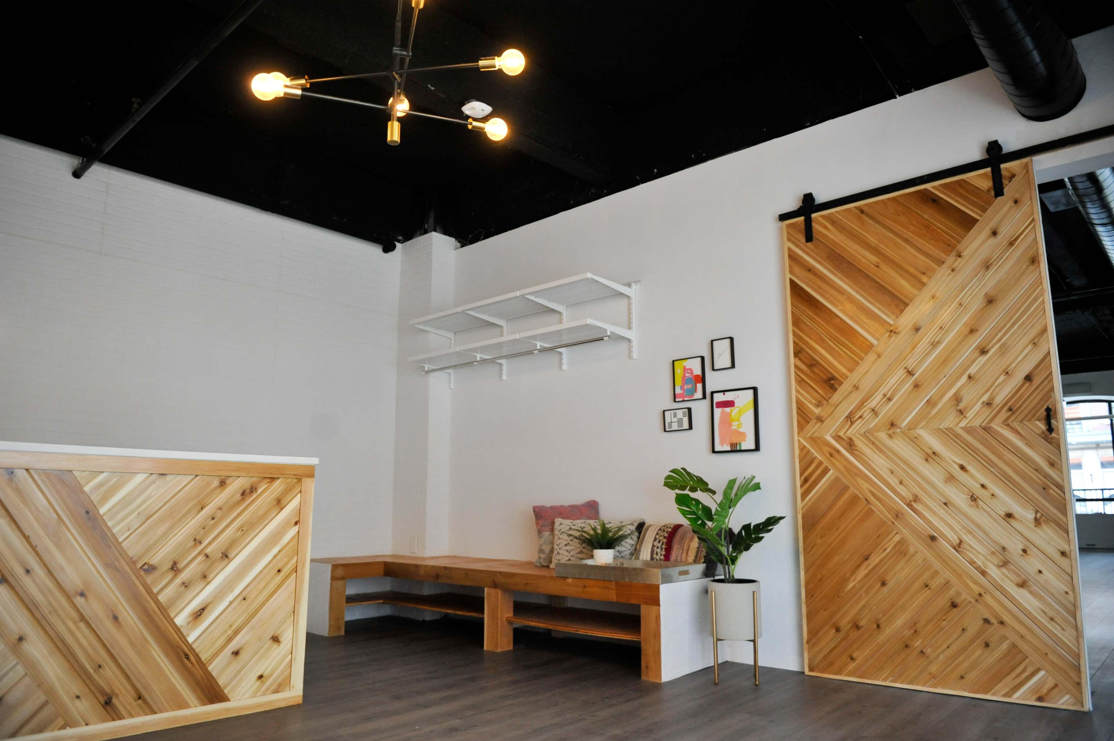 A modern reception area featuring a wooden counter, a seating bench, and a large sliding wooden door with a diagonal pattern.