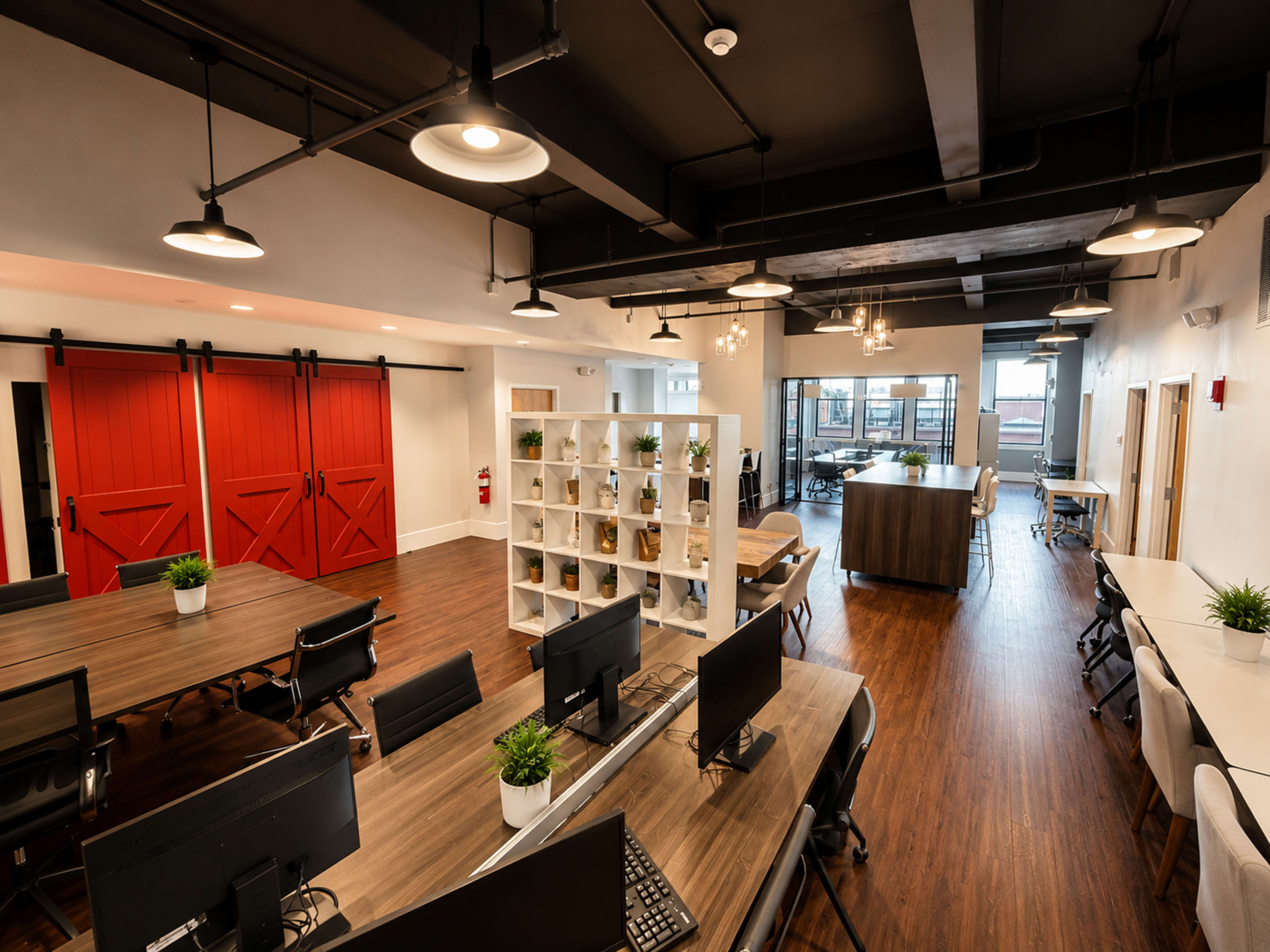 The image shows a modern office space featuring wooden flooring, workstations with computers, and a bright area with red sliding barn doors and stylish light fixtures.