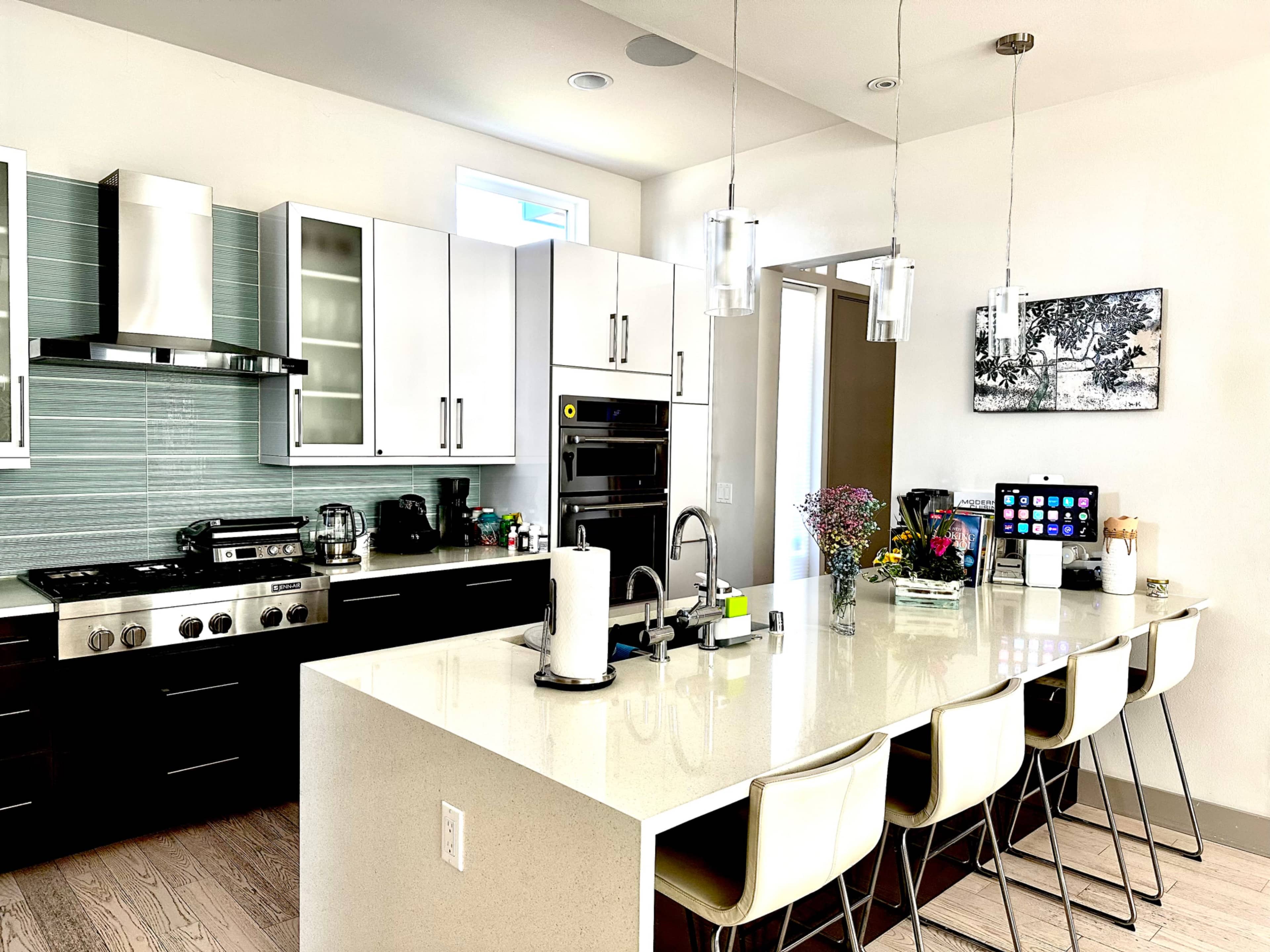 The kitchen features a modern design with a large island, stainless steel appliances, white cabinets, and a variety of countertop items.