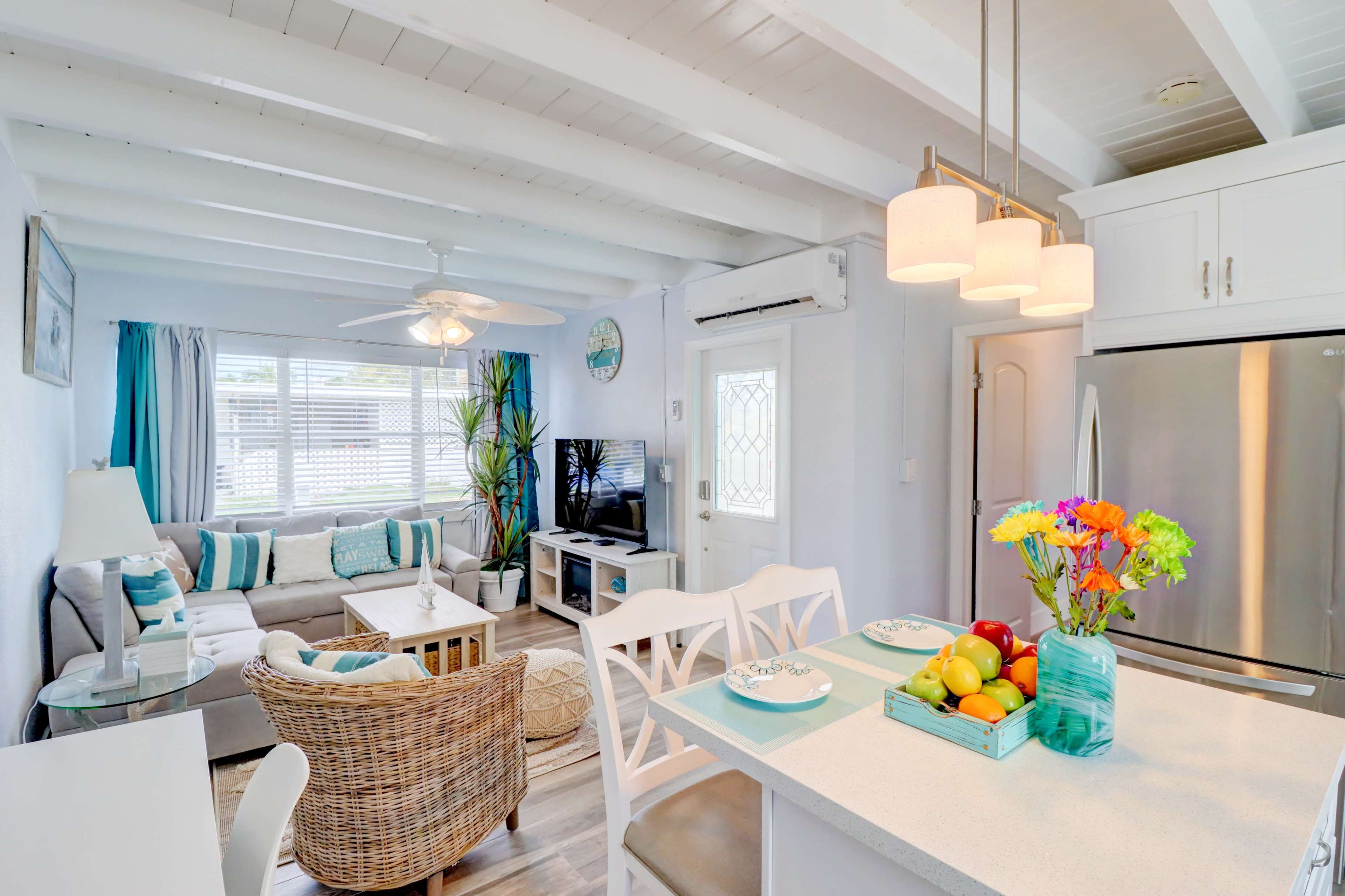 A bright, modern living room with a cozy sofa, a dining area featuring a table with fruit, and large windows letting in natural light.