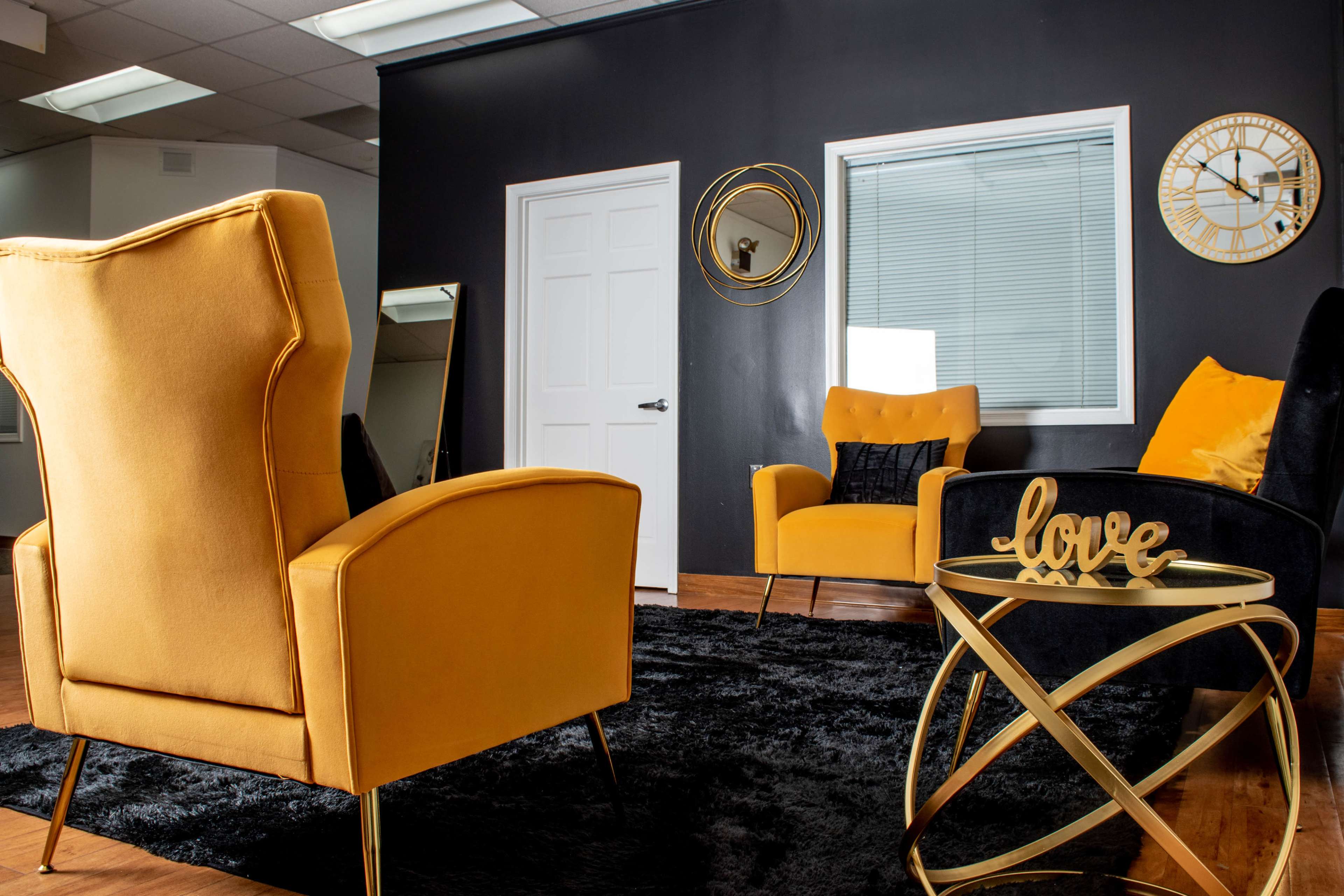 A modern interior with yellow upholstered chairs, a black rug, and a gold accent table displaying the word "love."