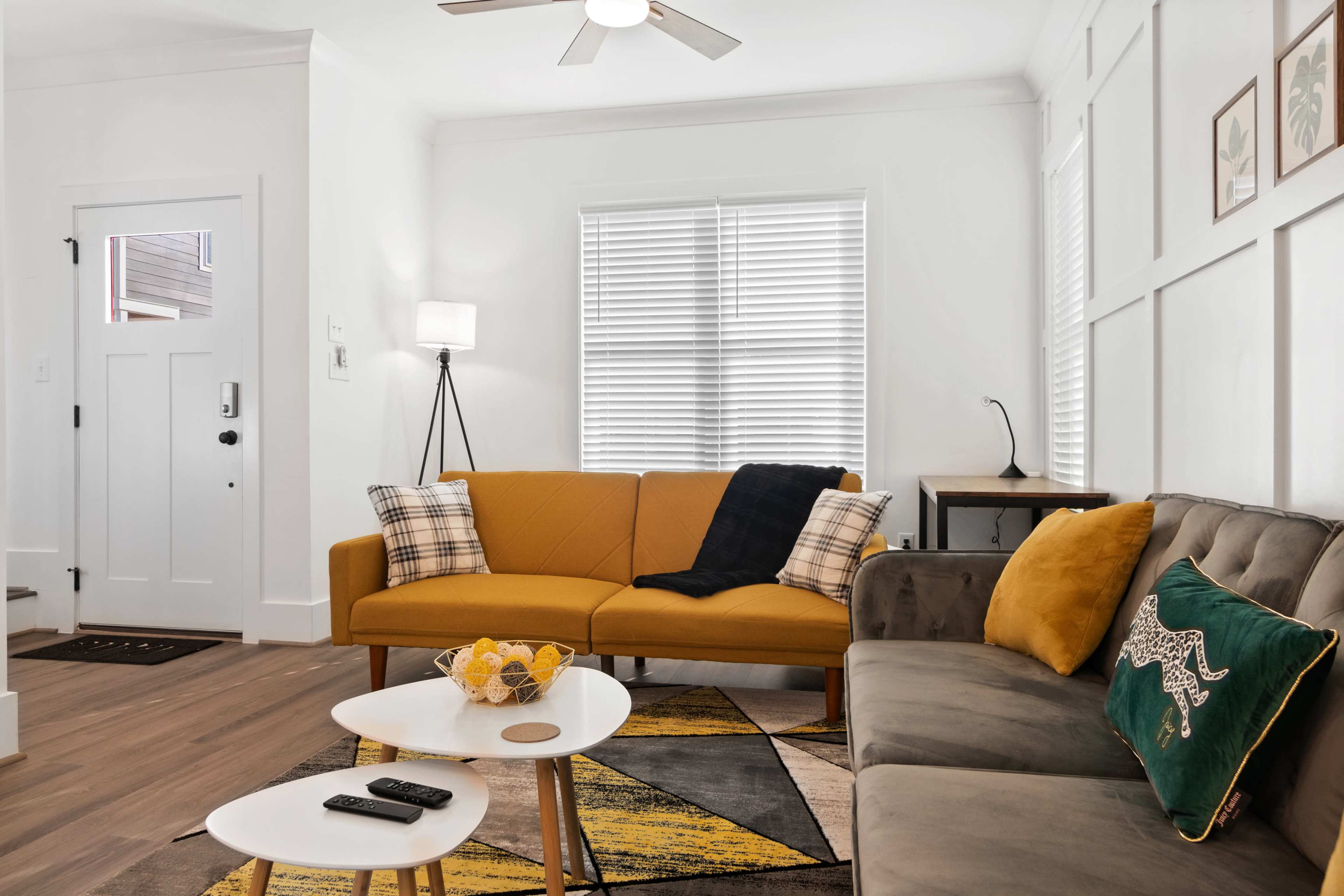 A modern living room featuring a yellow couch, a gray sofa, a coffee table, and a lamp, with large windows providing natural light.
