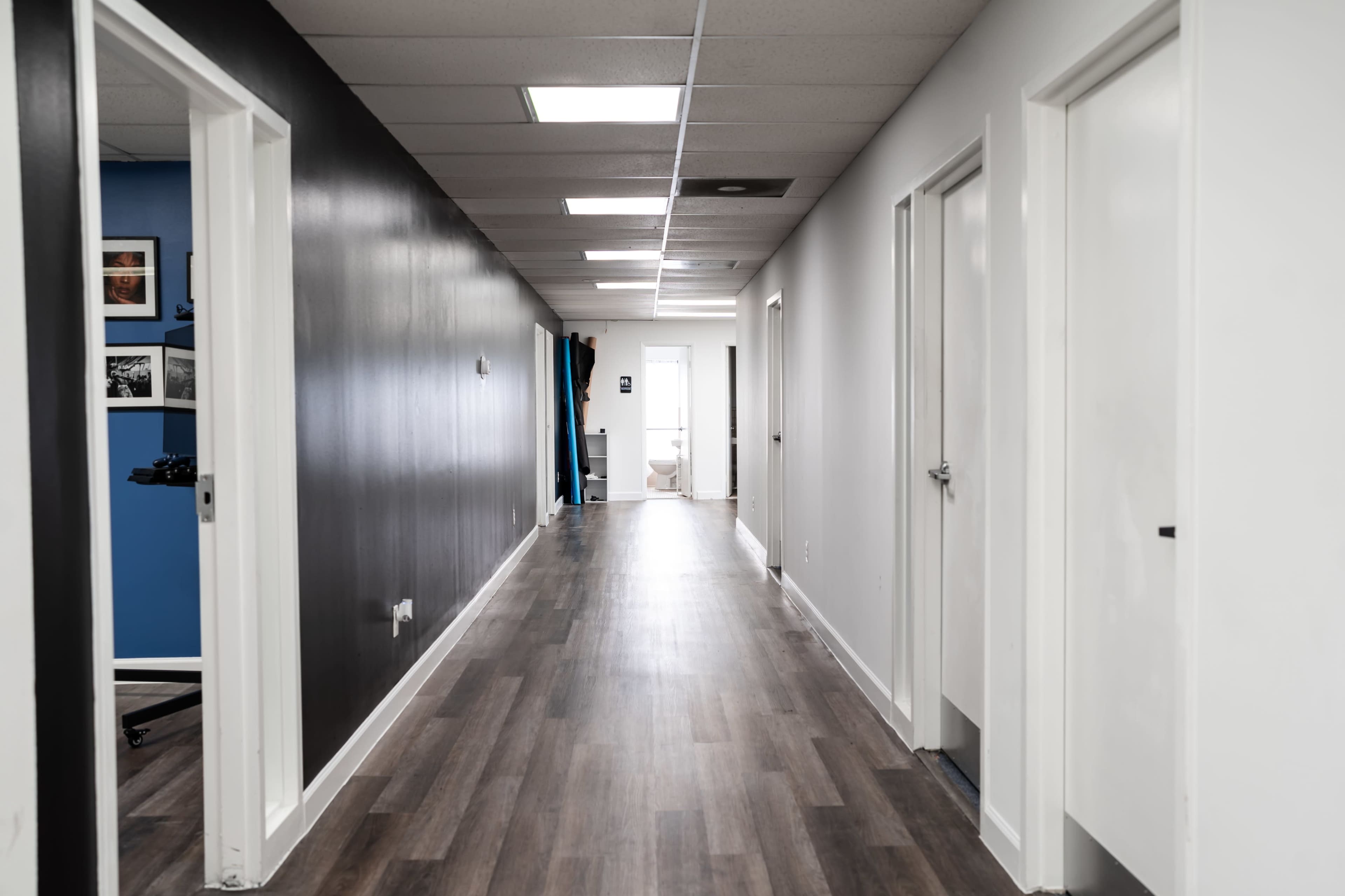 A long, narrow hallway with white and black painted walls and several closed doors on either side.