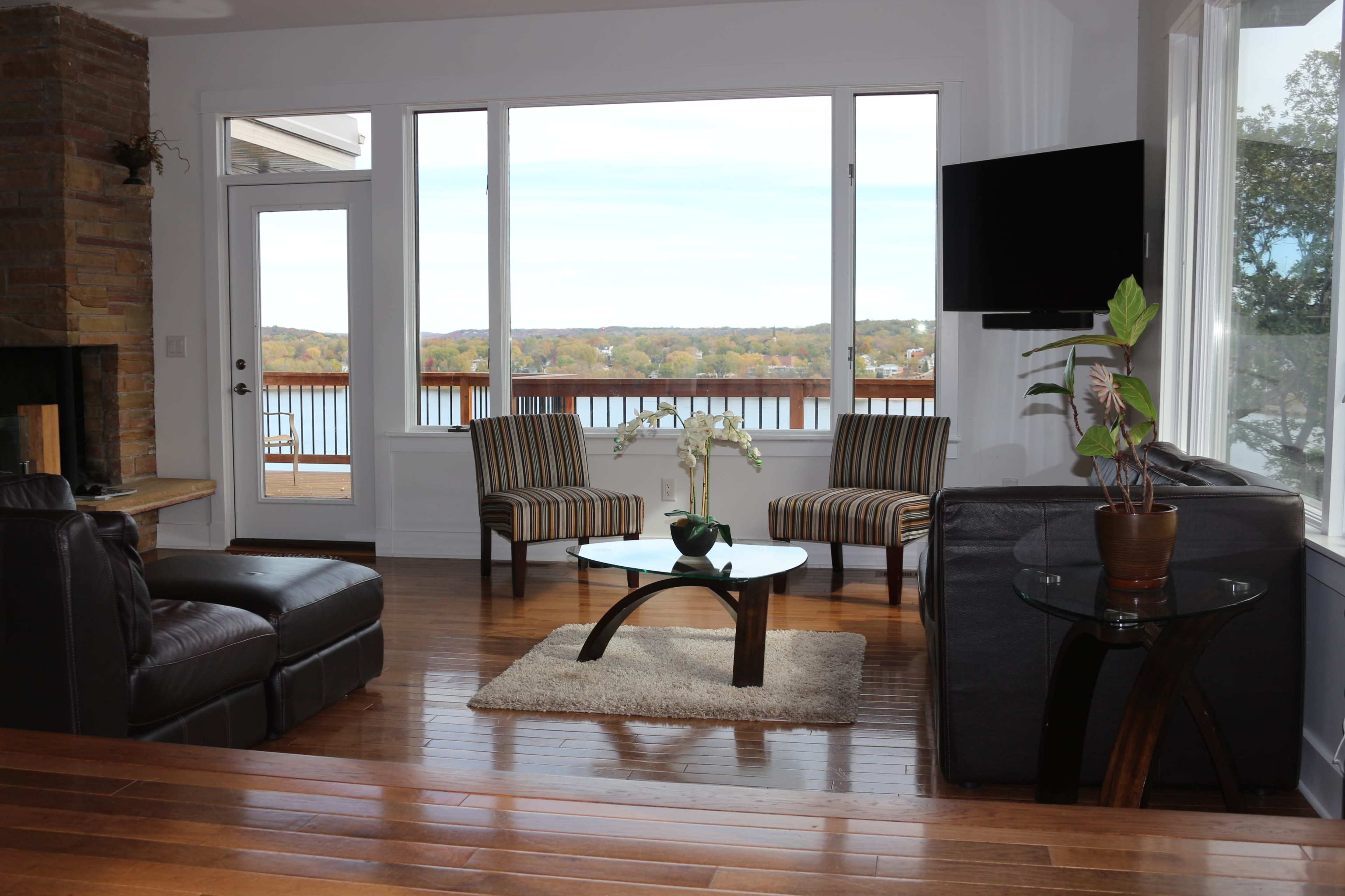 A living room with two striped chairs, a glass coffee table, and large windows overlooking a lake.