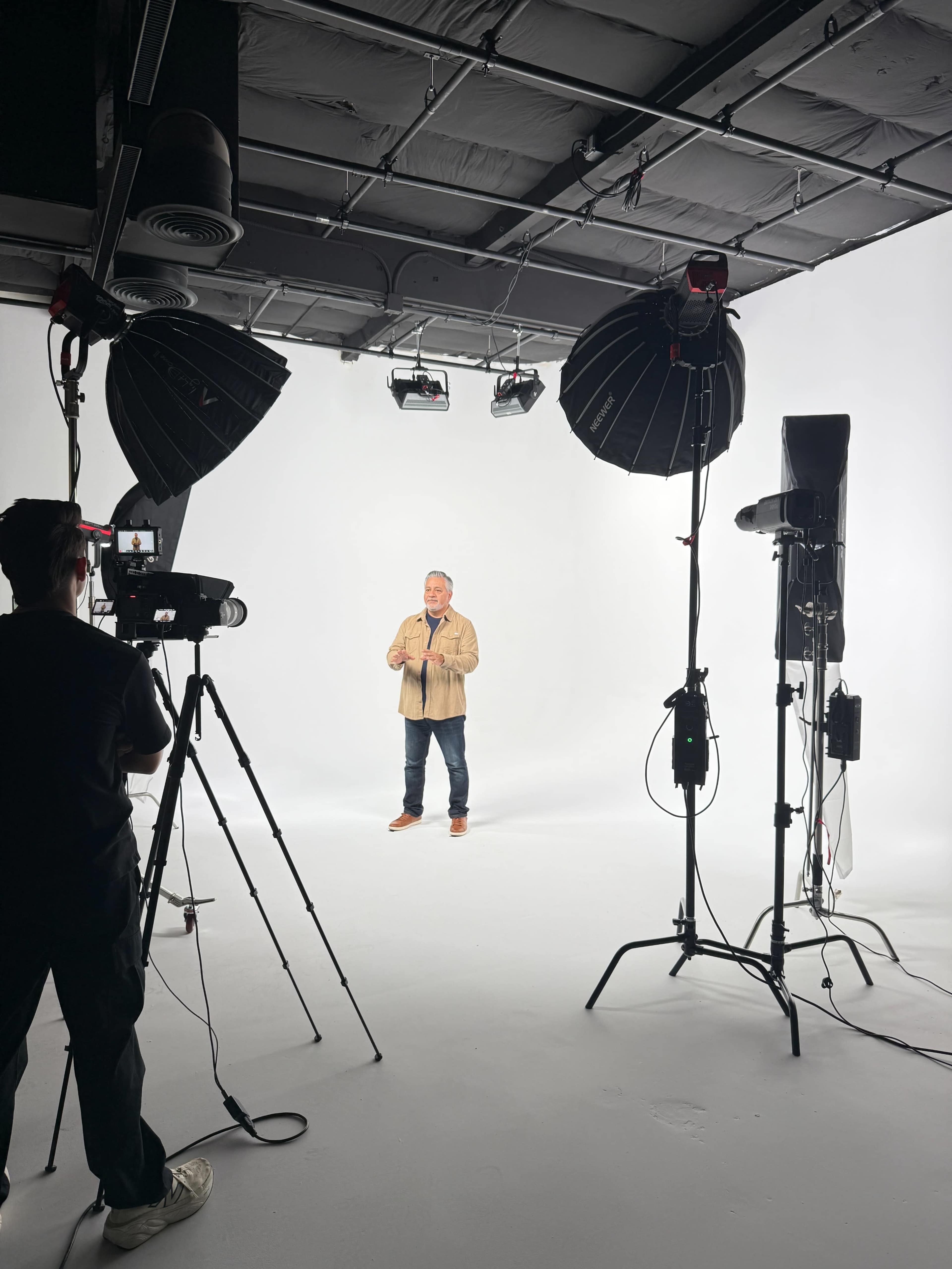 A man stands in front of a white backdrop in a studio, surrounded by professional lighting and cameras.