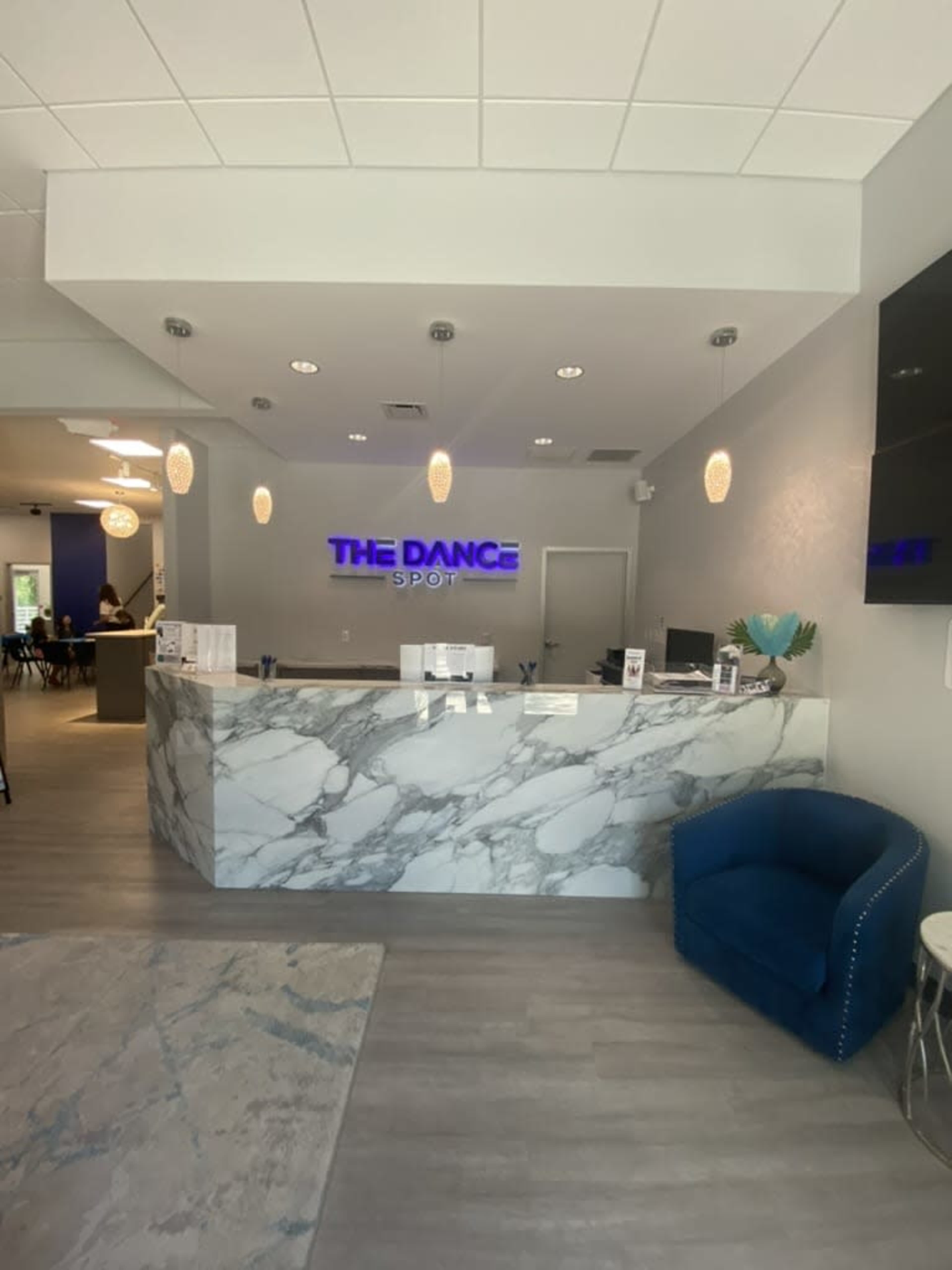 The image shows a reception area of a dance studio featuring a marble front desk, purple signage that reads "THE DANCE SPOT," and modern furnishings.
